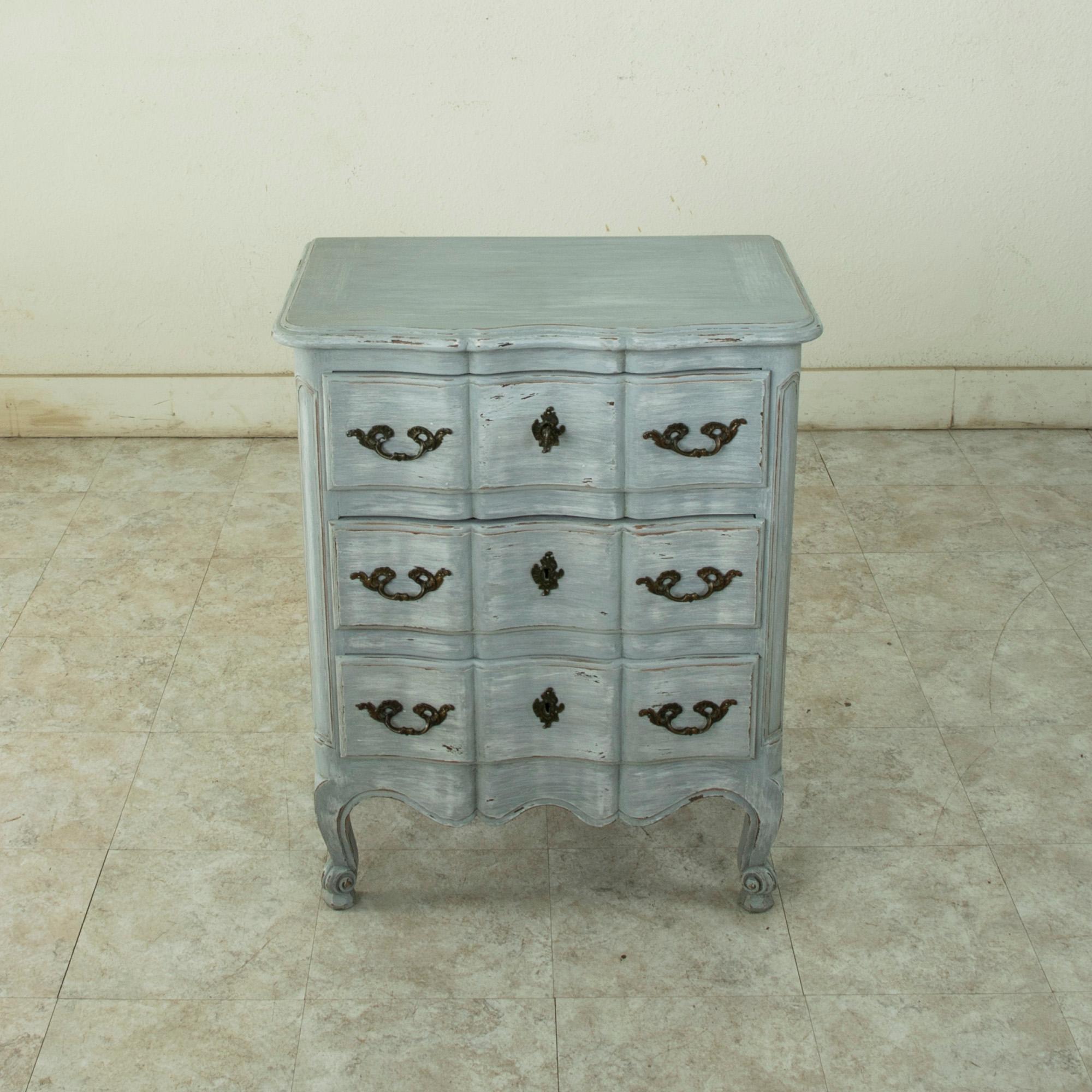 This small scale early twentieth century French Louis XV style beech wood commode or chest is painted in a worn pale blue-grey known as Marie Antoinette grey. Three drawers of dovetail construction feature curved fronts appointed with bronze drawer