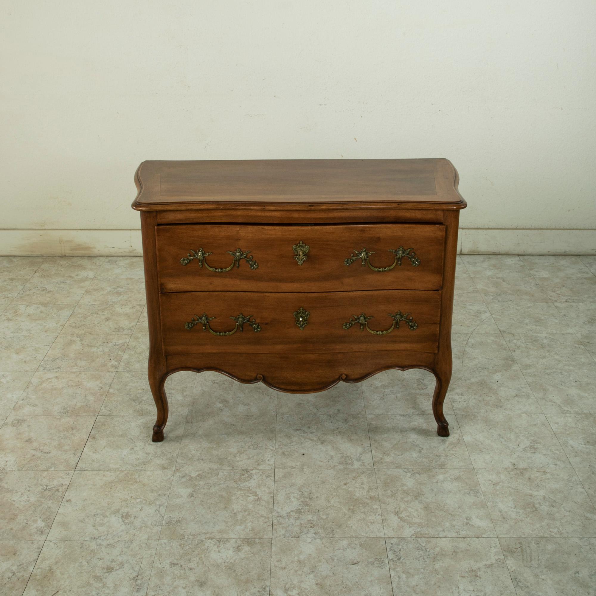 This early twentieth century French Louis XV style commode or chest of drawers is constructed of solid walnut. This piece is called a sauteuse in French, or jumping chest, due to its high legs. The chest features a beveled top and curved sides, and