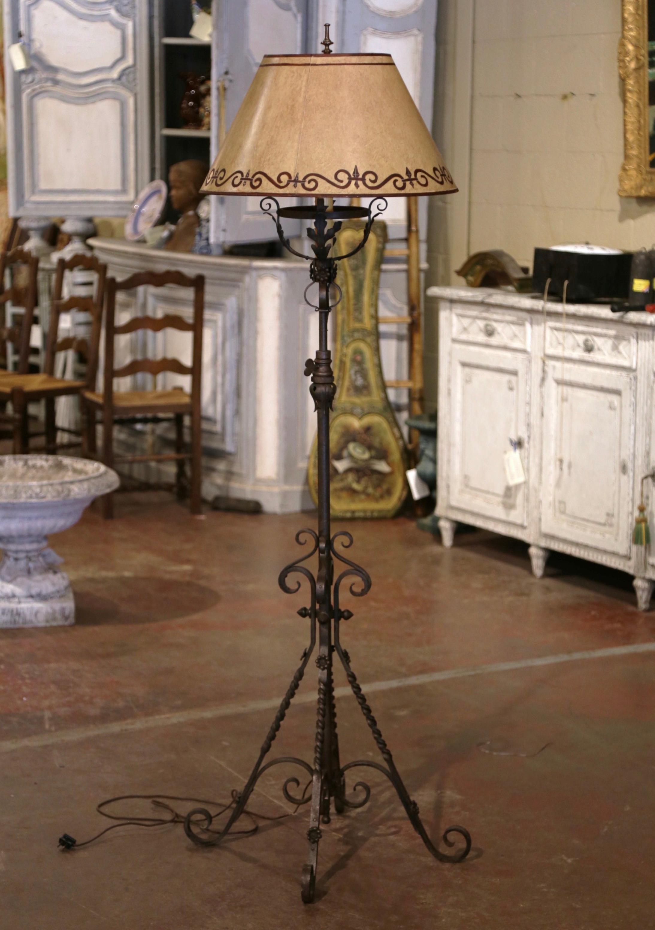 This tall iron floor lamp was created in Southern France circa 1920. Standing on a pedestal ending with four scrolled and twisted feet, and decorated with floral rosettes, the lamp features an intricate stem decorated with a center mount and