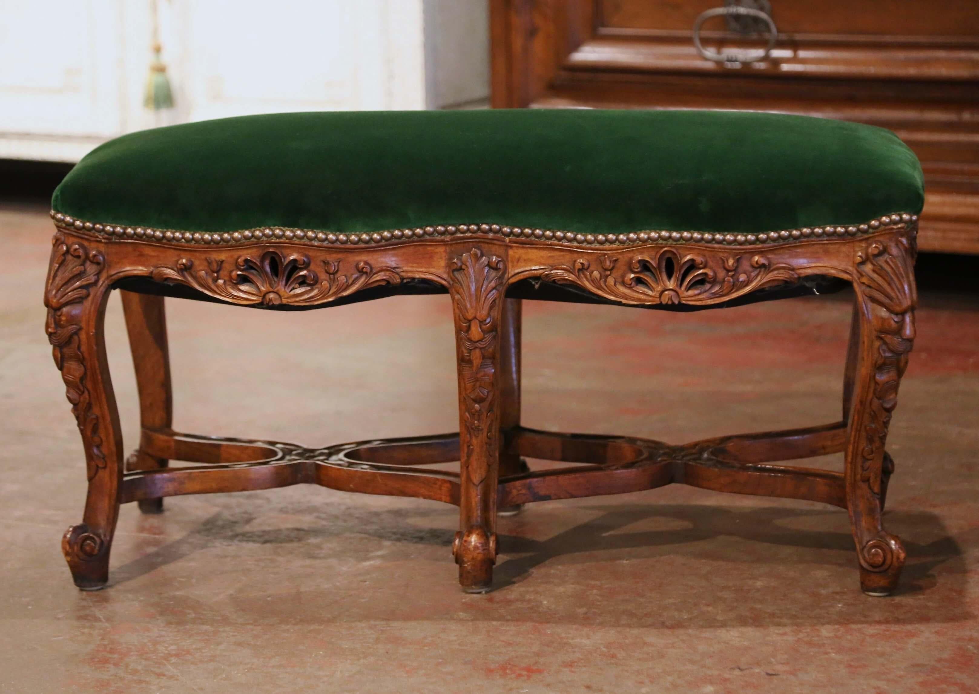 Crafted in Provence, France circa 1920, the antique fruitwood bench stands on six cabriole legs and escargot feet over a curved stretcher at the base; each leg is further decorated with hand carved acanthus leaf and face motifs at the shoulder. The