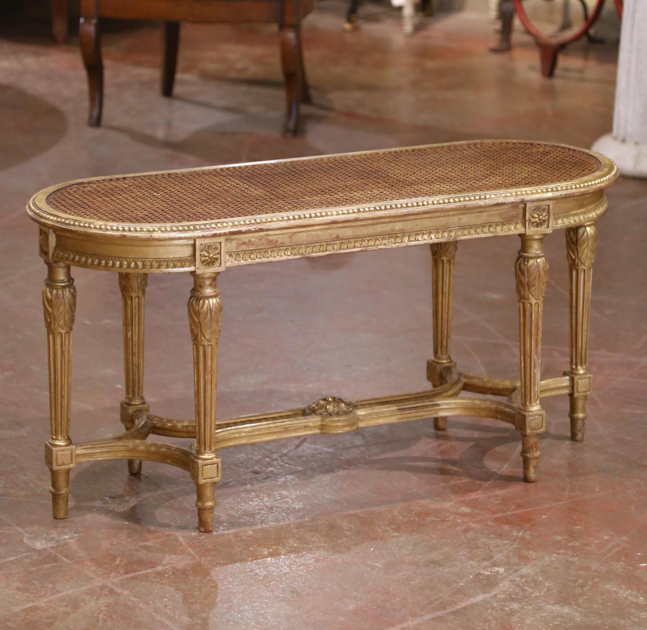 Raffiné et élégant, ce banc ancien a été fabriqué en France vers 1920 dans le style Louis XVI et présente un bois doré magnifiquement sculpté et une assise cannée à la main. Le cadre ovale est orné d'une bordure perlée et de motifs d'acanthe