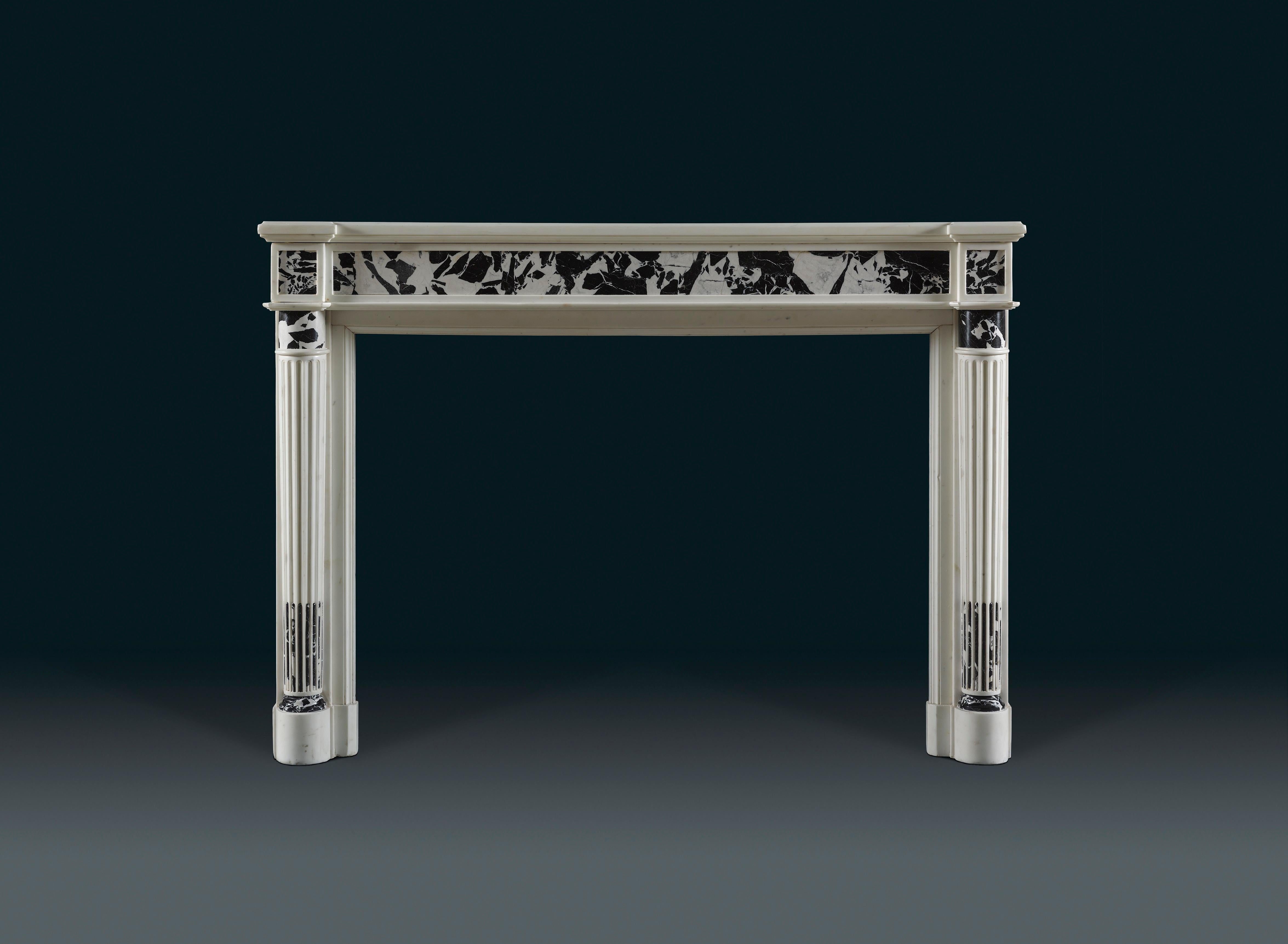 Of typical rectangular form, of statuary and black and white 'Grande Antique' marble.

The oblong moulded shelf protruding over the jamb blockings, the frieze with a well figured inlaid panel of Grande Antique flanked by the protruding blockings