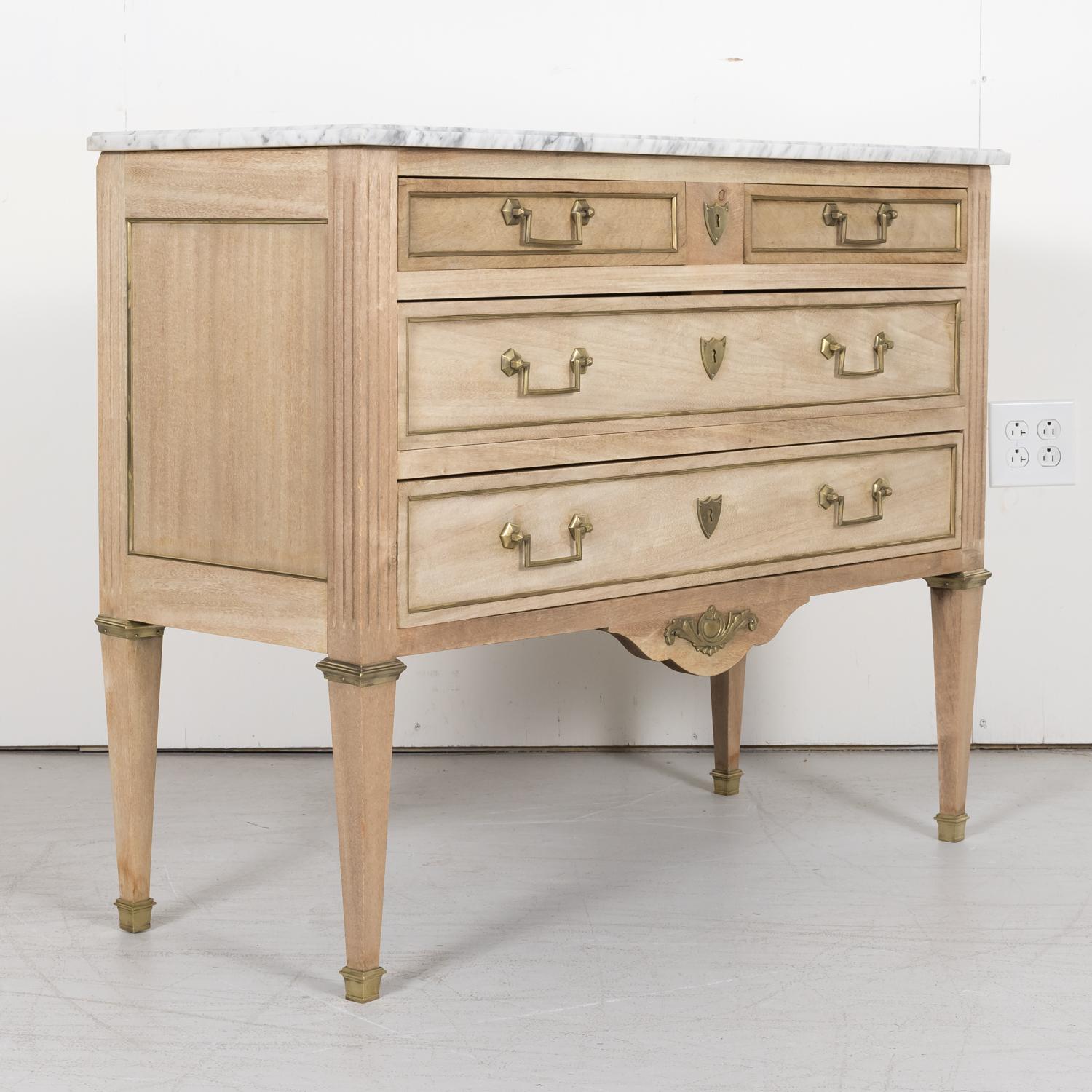 An early 20th century French Louis XVI style bleached mahogany four drawer commode handcrafted in Paris, circa 1900, having its original Carrara marble top over two frieze drawers above two long drawers adorned with original brass trim, drop bail