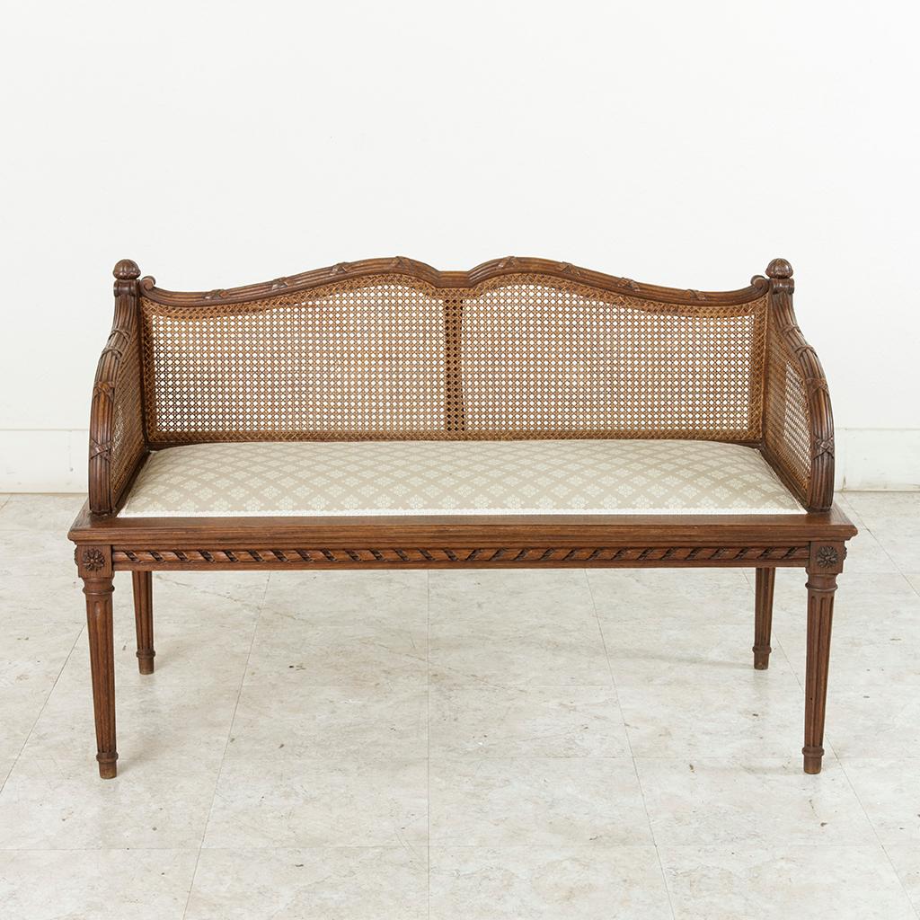 This beautifully carved oak banquette or bench in the Louis XVI style features a caned seat back and arms, all in pristine condition. The seat was recently reupholstered in France with a Pierre Frey fabric. Classic Louis XVI twisted ribbon surrounds