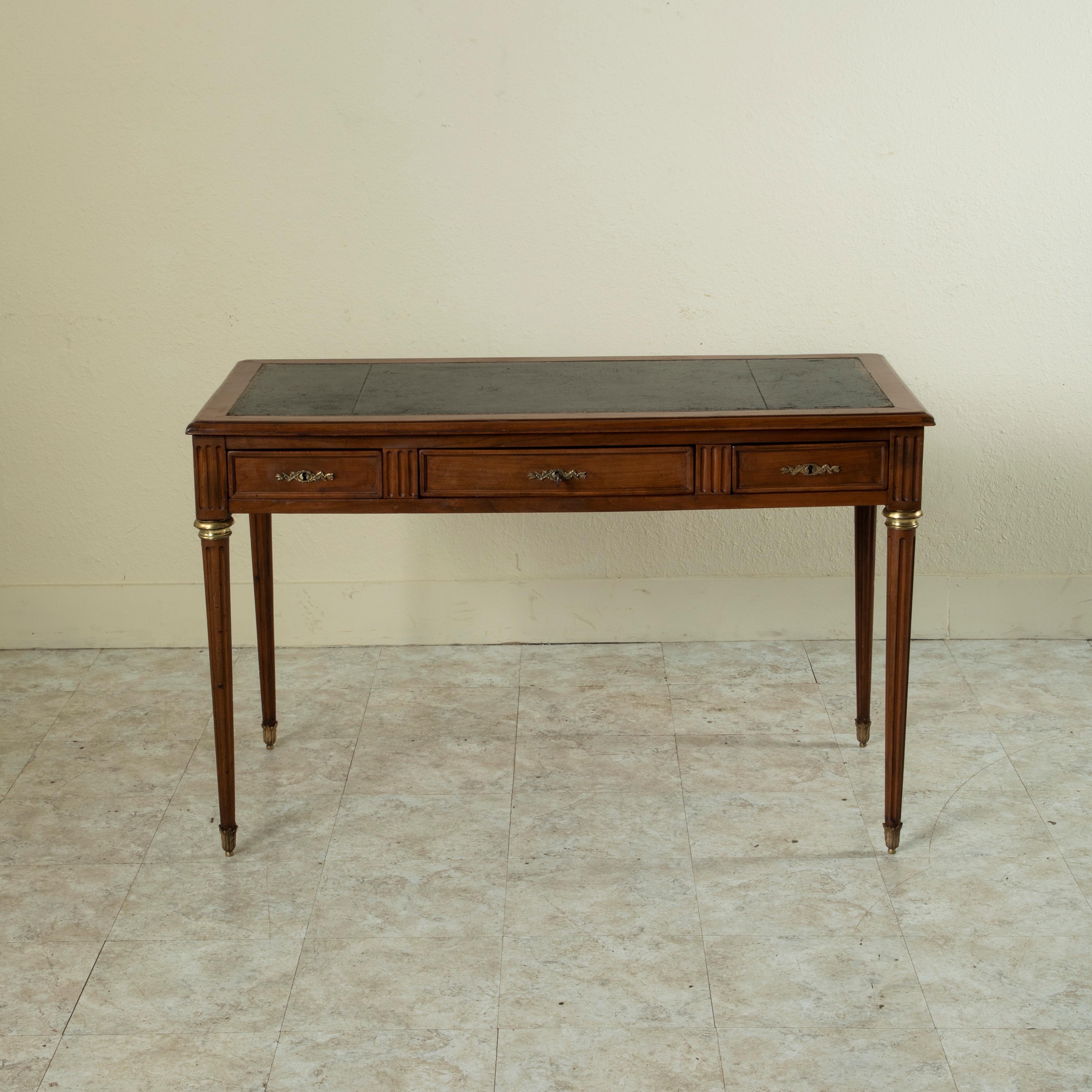 This early twentieth century French Louis XVI style cherry wood writing desk features a gold tooled black leather top and two leather top trays that pull out on the sides. Three drawers of dovetail construction are fitted with bronze escutcheons