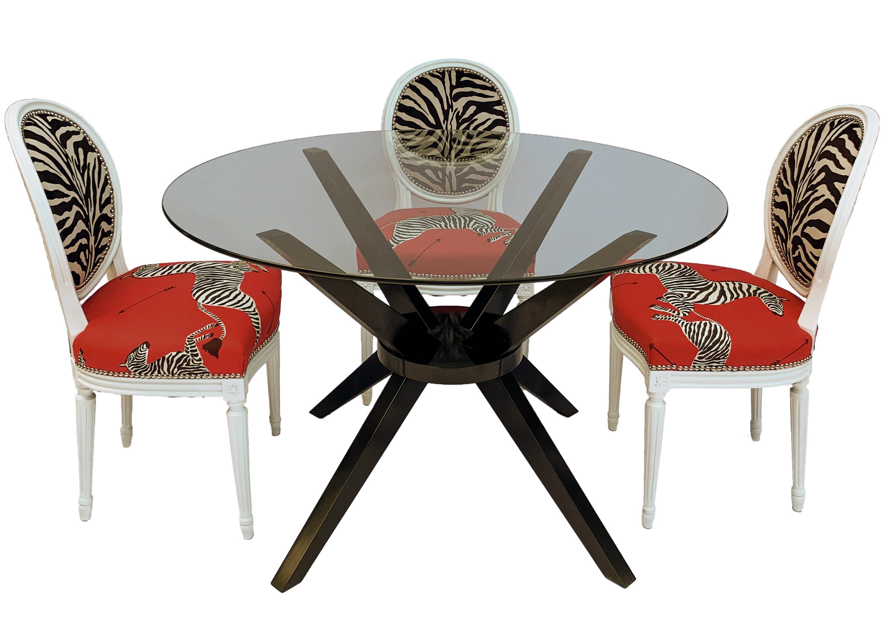Early 20th century French Louis XVI style dining chairs with modern dining table. The chairs have been lacquered white and the glass top wood table base lacquered in black. The chairs have been reupholstered in Scalamandre’s iconic red masai zebra