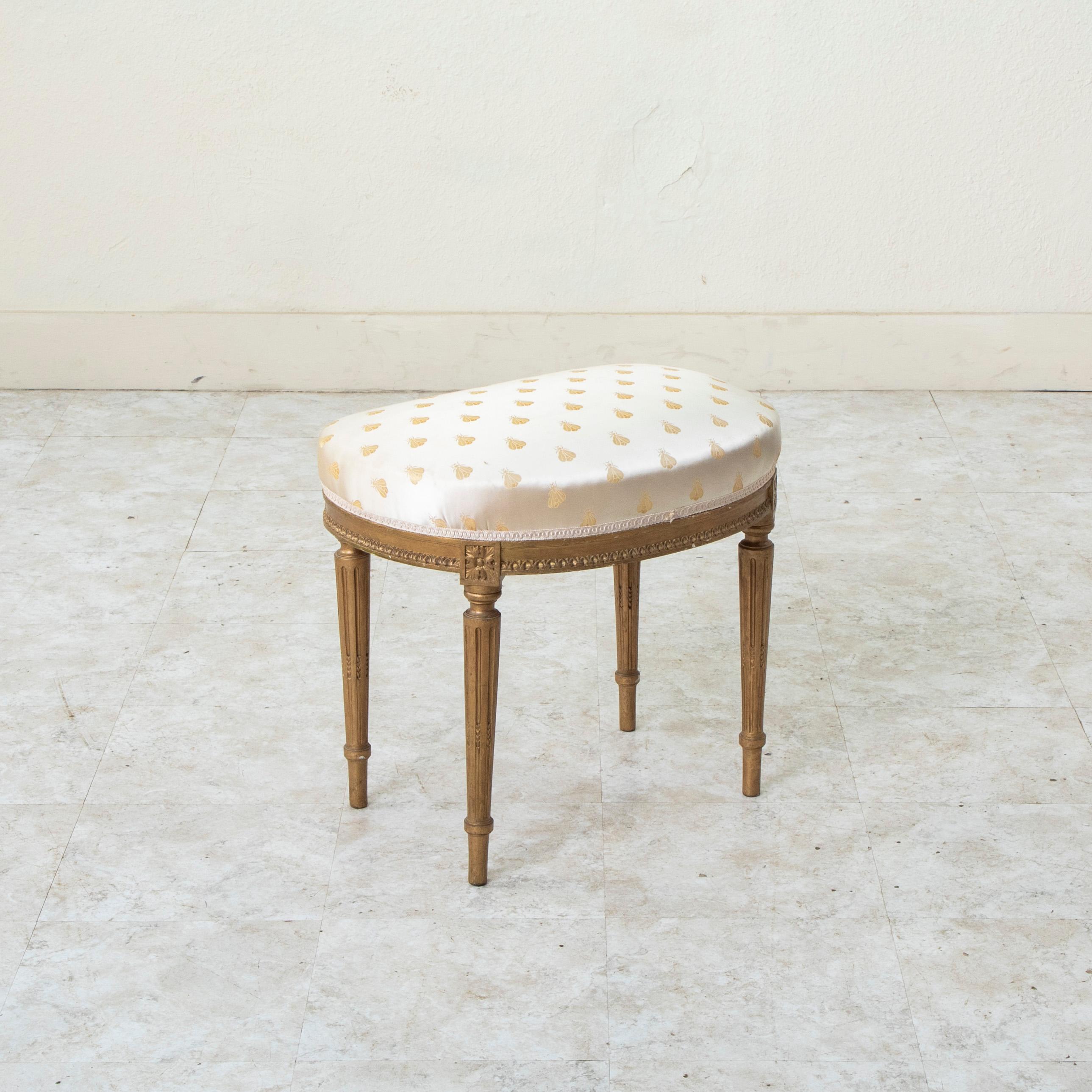This early twentieth century French Louis XVI style kidney shaped vanity stool features hand carved detailing of rosettes at the die joints and a rais-de-coeur pattern along the apron. The seat rests on four tapered cable fluted legs and is