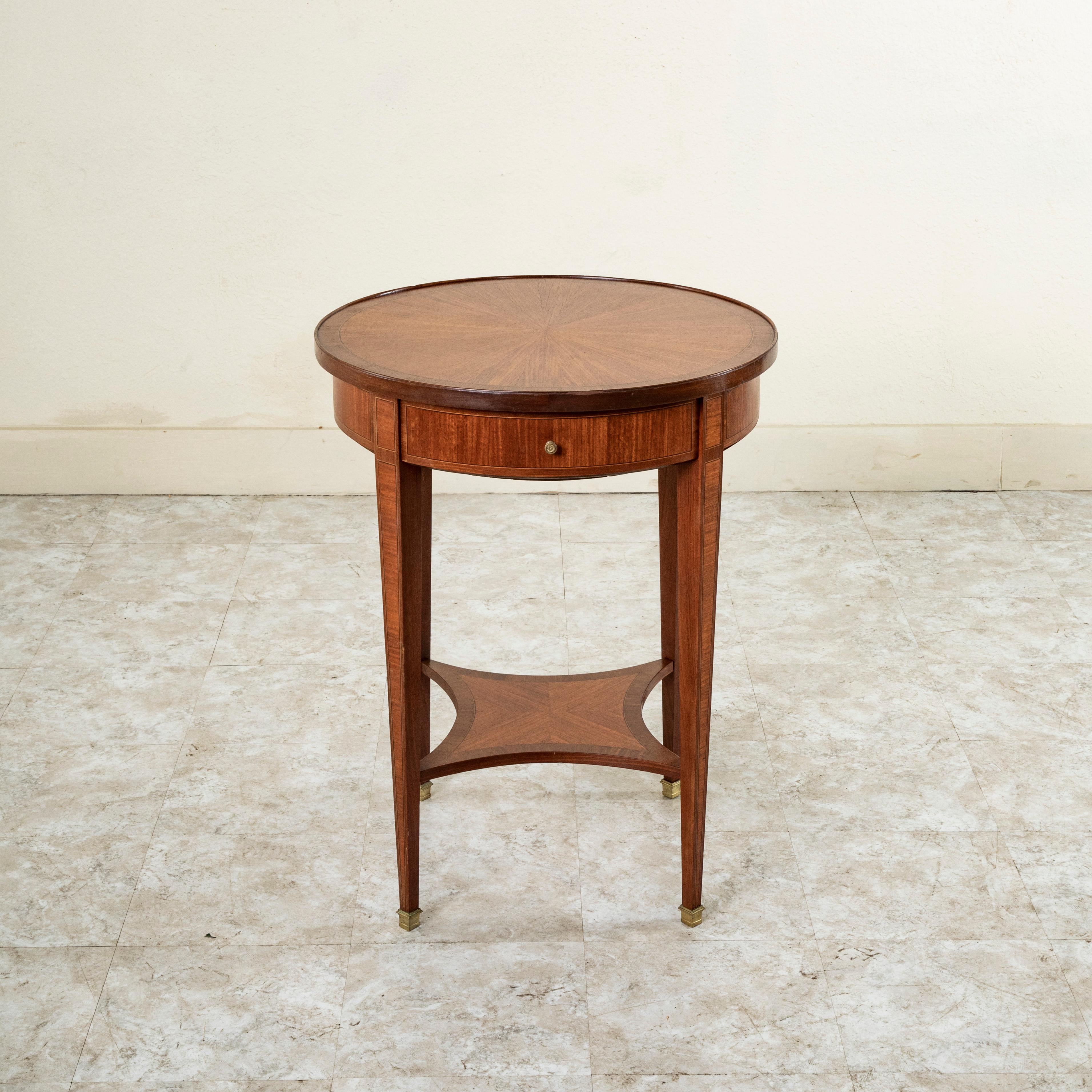 This early 20th century French Louis XVI style round rosewood side table features an marquetry top in a sunburst pattern with an inset border of fine lines of lemon wood and ebonized pearwood. The inset border pattern is repeated on the apron below
