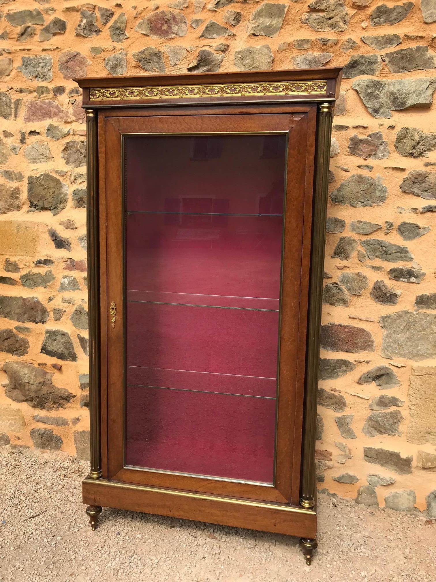 Early 20th century French mahogany and gilted brass directoire style vitrine.
Spindle feet, fluted columns with brass.
Three glass shelves and glass sides. Lining fabric was probably added later.
The crest is decorated with brass garland