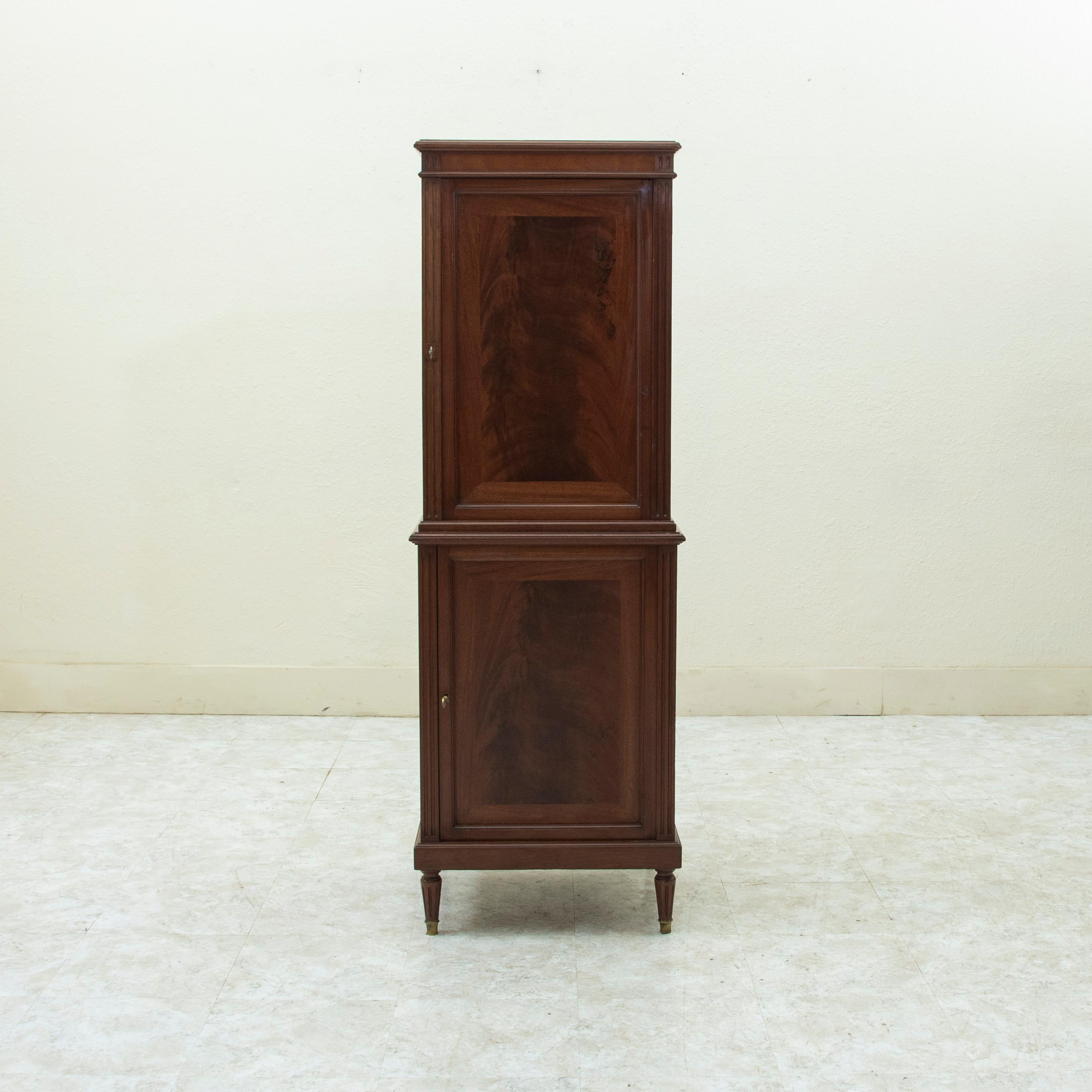 Standing at 57.75 inches in height with only a 19.75 inch width, this French mahogany cabinet from the turn of the twentieth century features an upper and lower section, each with a door flanked by fluted corners. Each door opens using its using its