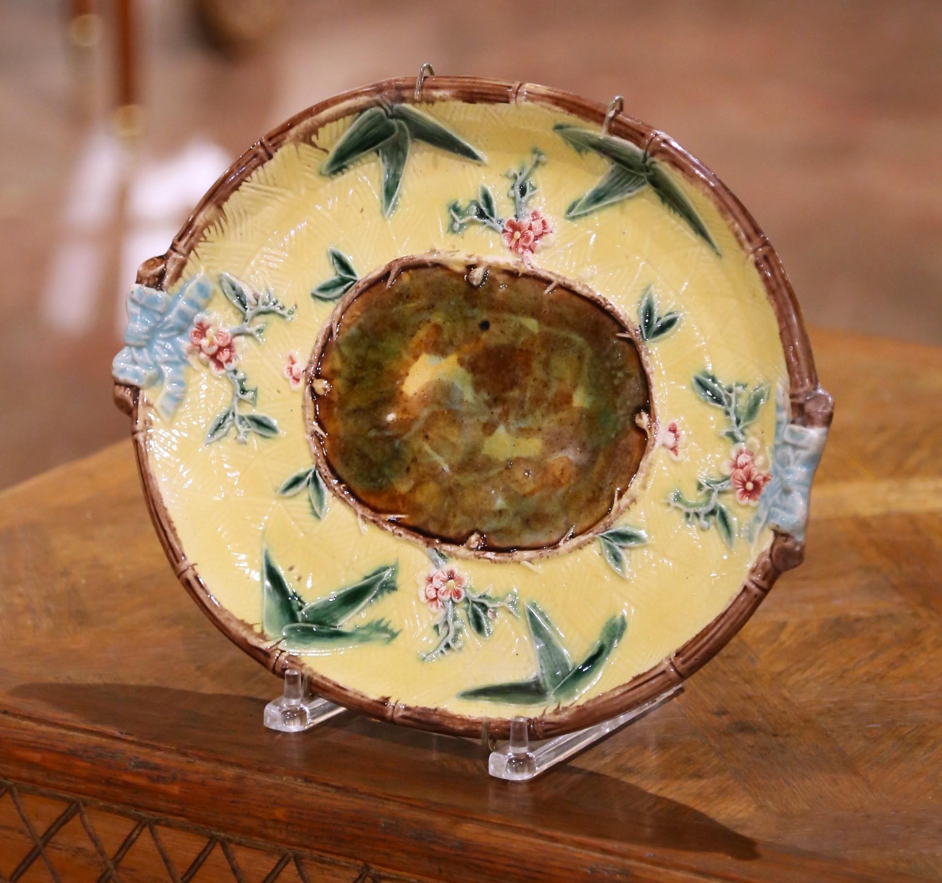 Fabriqué en France vers 1920, ce charmant plat à suspendre met en valeur l'art de la céramique française du début du XXe siècle. Le plat ovale est décoré en majolique à glaçure brillante, avec un fond central marbré brun et vert encadré d'une