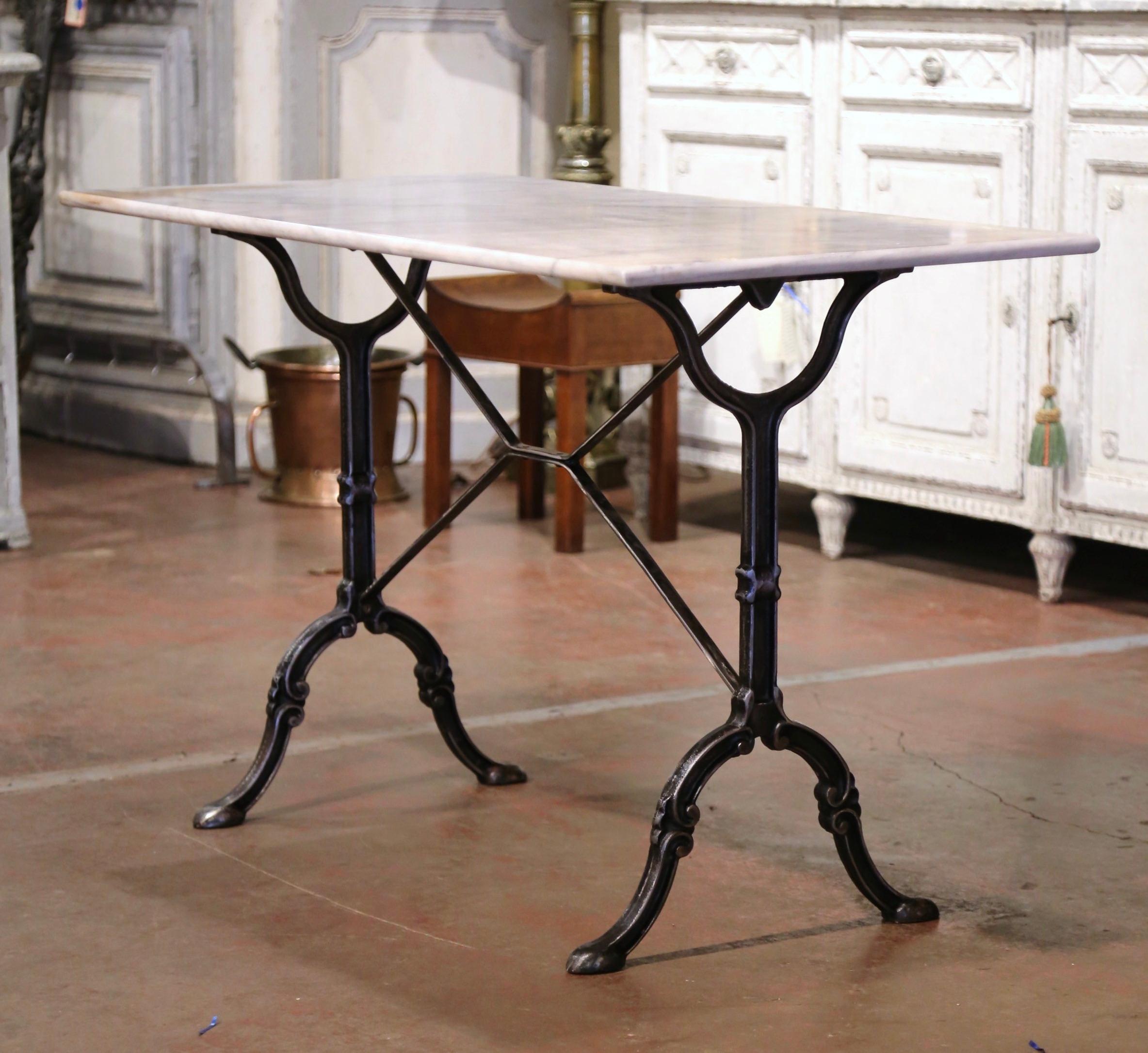 Crafted in France circa 1960, the antique cast iron table sits on a trestle base with elegant scroll legs ending with hoof feet, and joined together with a double decorative stretcher. The piece is dressed with the original rectangular white and