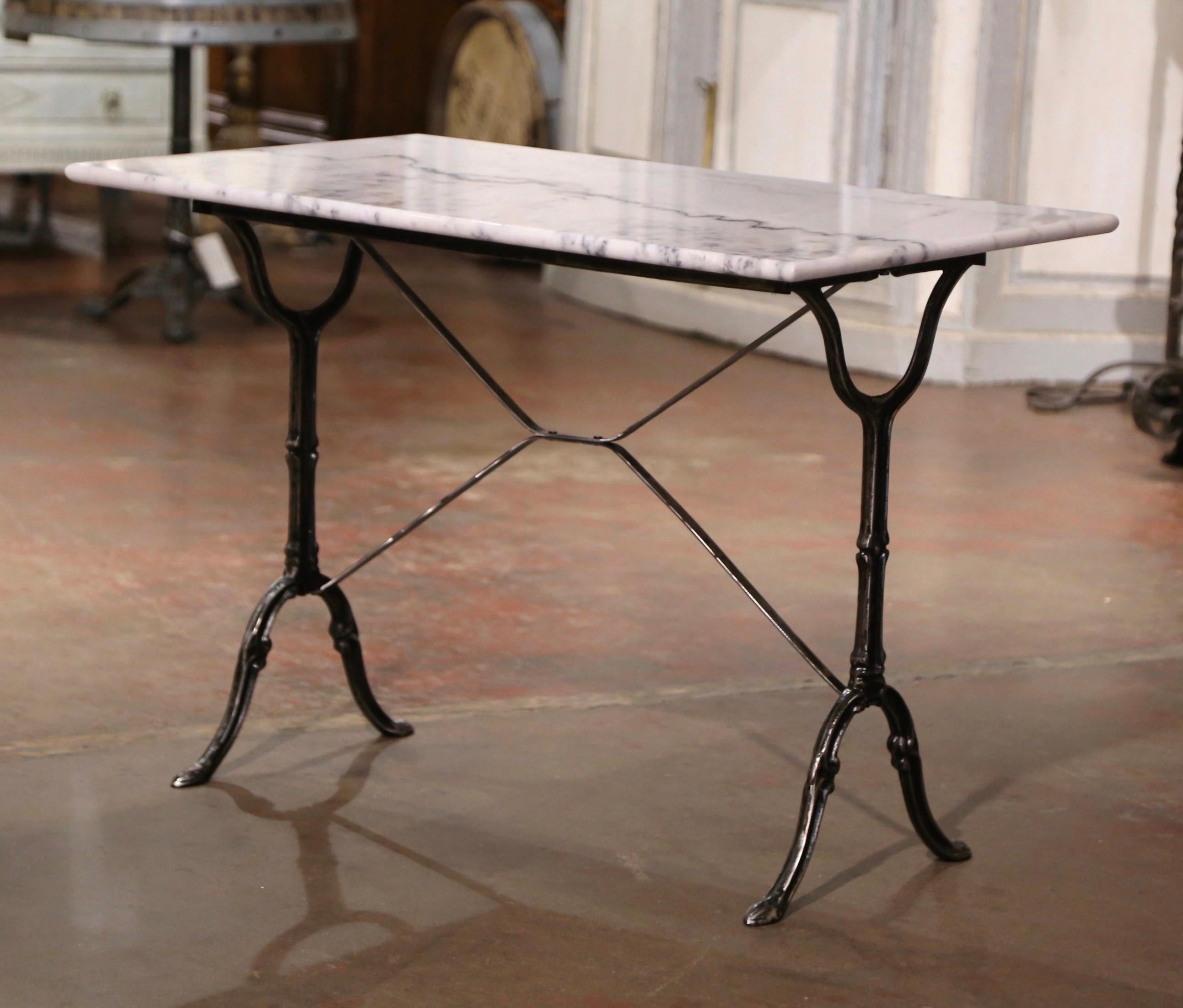 Crafted in France circa 1960, the antique cast iron table sits on a trestle base with elegant scroll legs ending with hoof feet, and joined together with a double decorative stretcher. The piece is dressed with the original rectangular white and