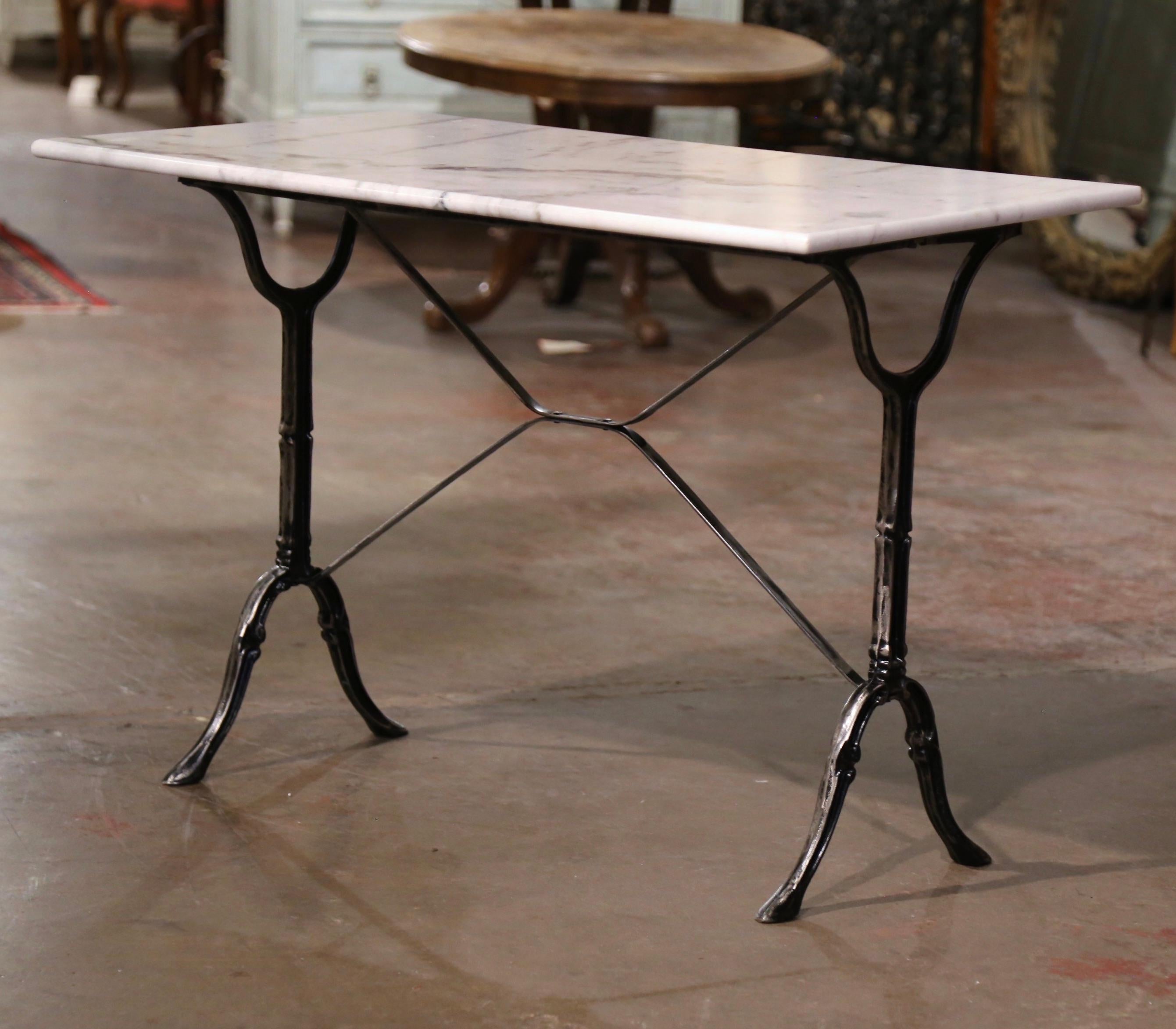 Crafted in France circa 1930, the antique table sits on a cast iron trestle base with elegant scrolled legs ending with hoof feet, and joined together with a double decorative stretcher. The table is dressed with the original rectangular white and