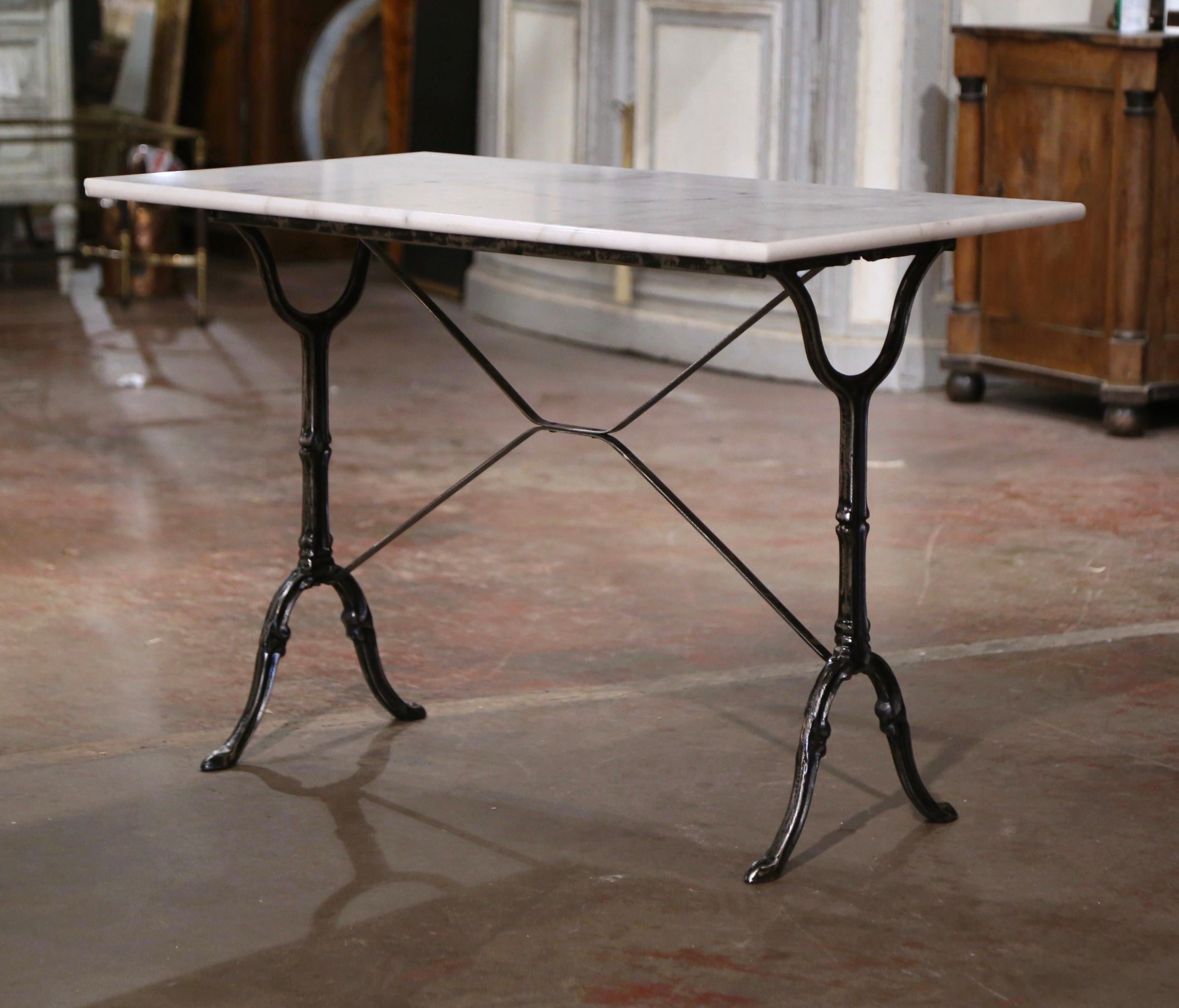 Crafted in France circa 1930, the antique table sits on a cast iron trestle base with elegant scrolled legs ending with hoof feet, and joined together with a double decorative stretcher. The table is dressed with the original rectangular white and