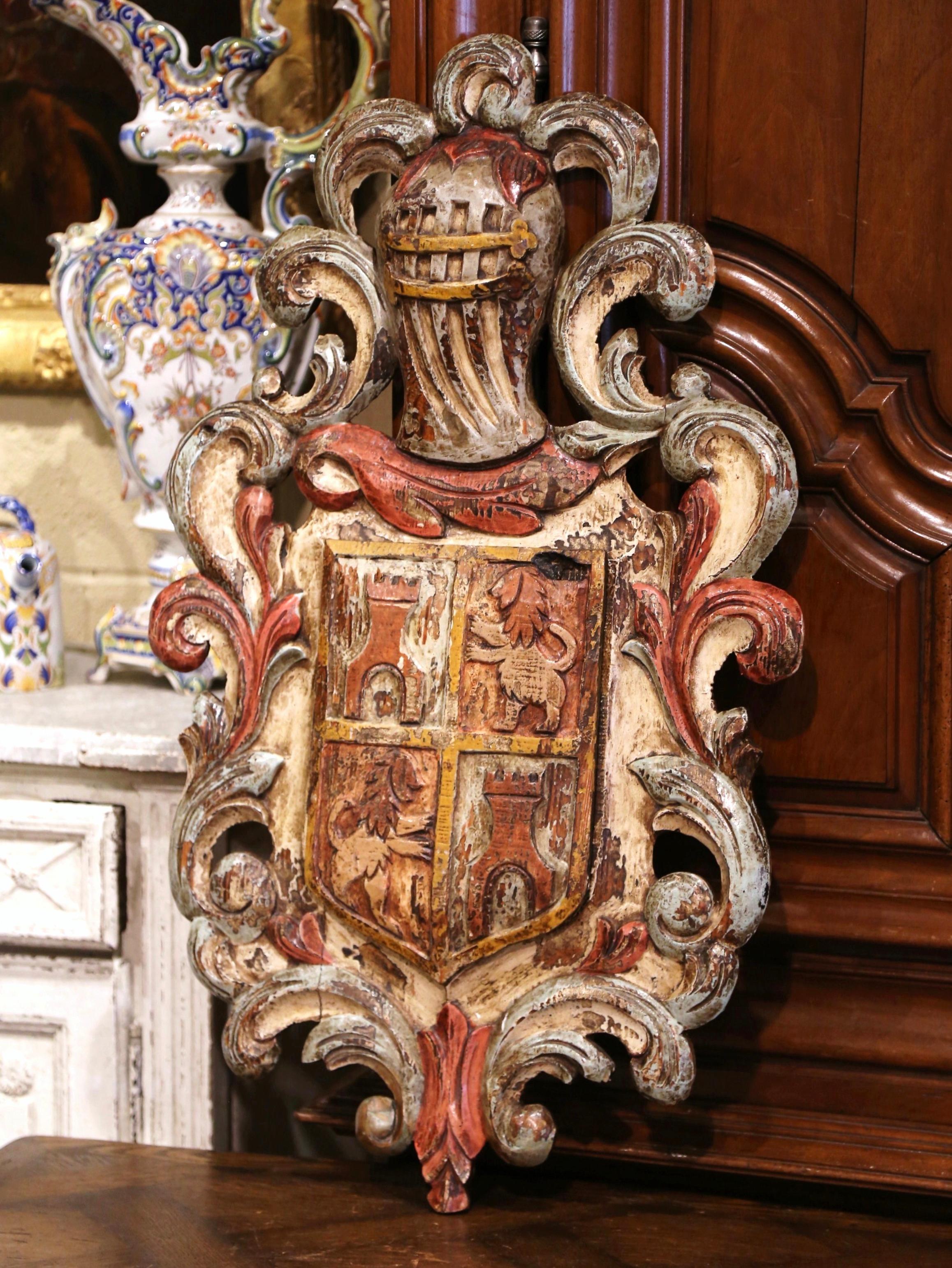 Embellish a study or office with this large antique medieval crest. Hand-carved in France, circa 1920, the hand painted shield with scroll and leaf motifs throughout, features a thick medieval helmet from a suit armor at the pediment; the center is