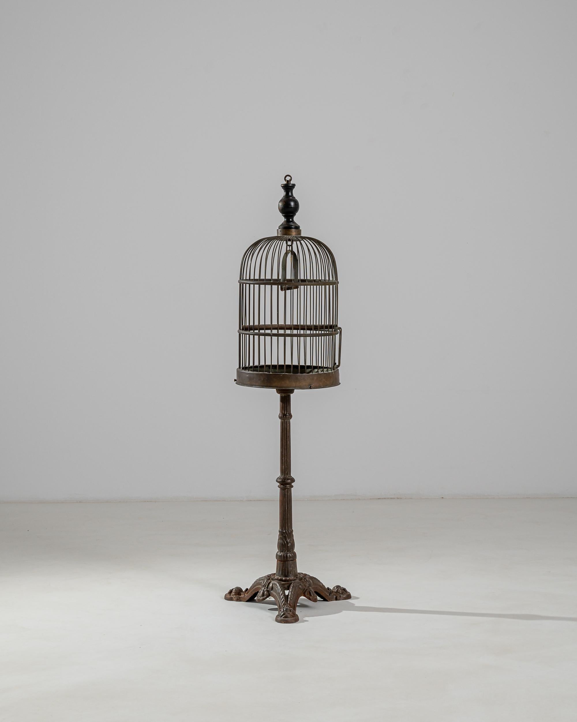A metal birdcage produced in France circa 1900. Elevated on a sculptural stand with richly molded tripod legs, this vintage birdcage has an oval dome topped with a pointed finial that elegantly punctuates the rounded silhouette of the cupola.