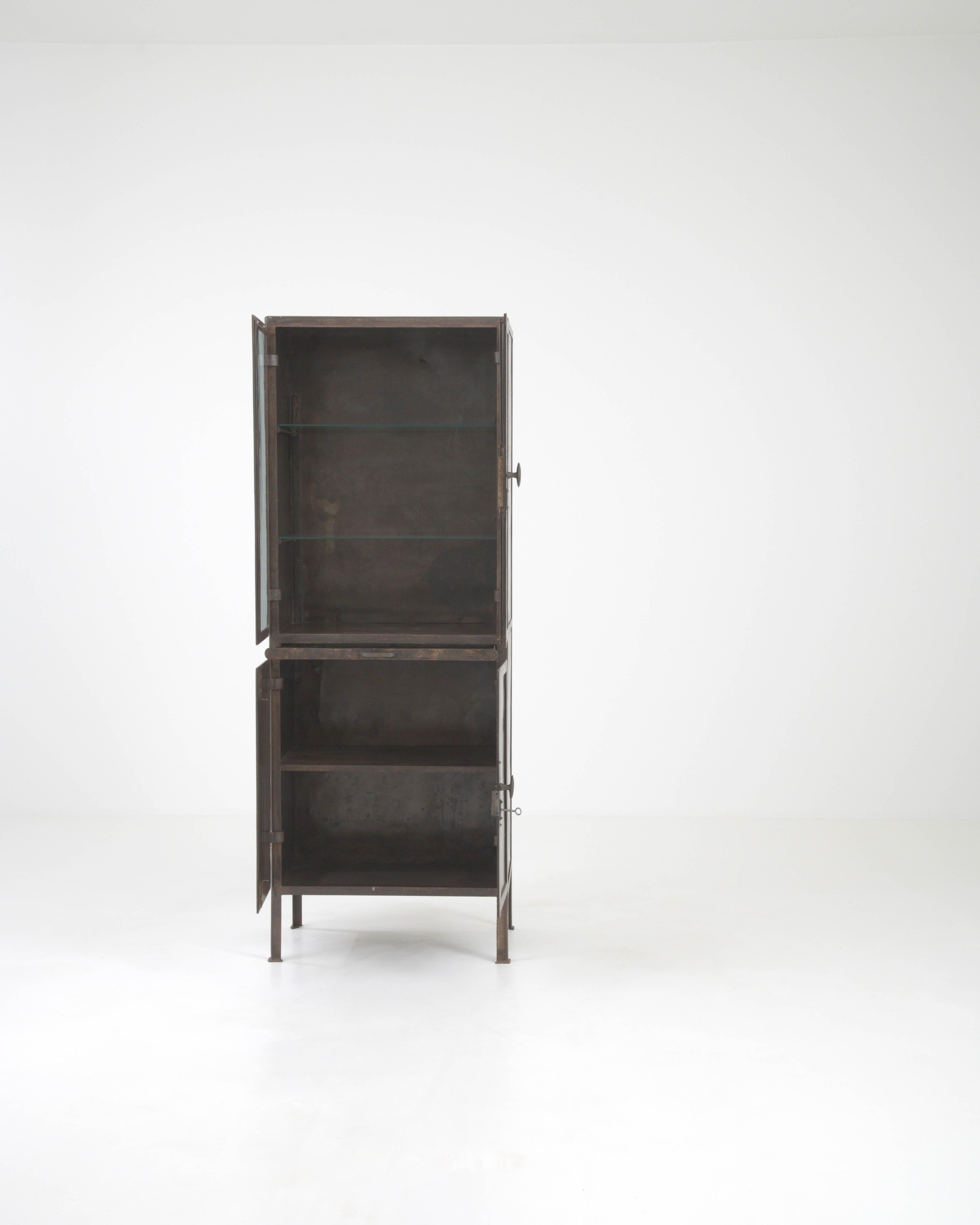 Immerse yourself in the bygone era of French elegance with this Early 20th Century French Metal Vitrine. A true statement piece, this cabinet showcases a rich history with its naturally weathered patina and classic silhouette. Designed to capture