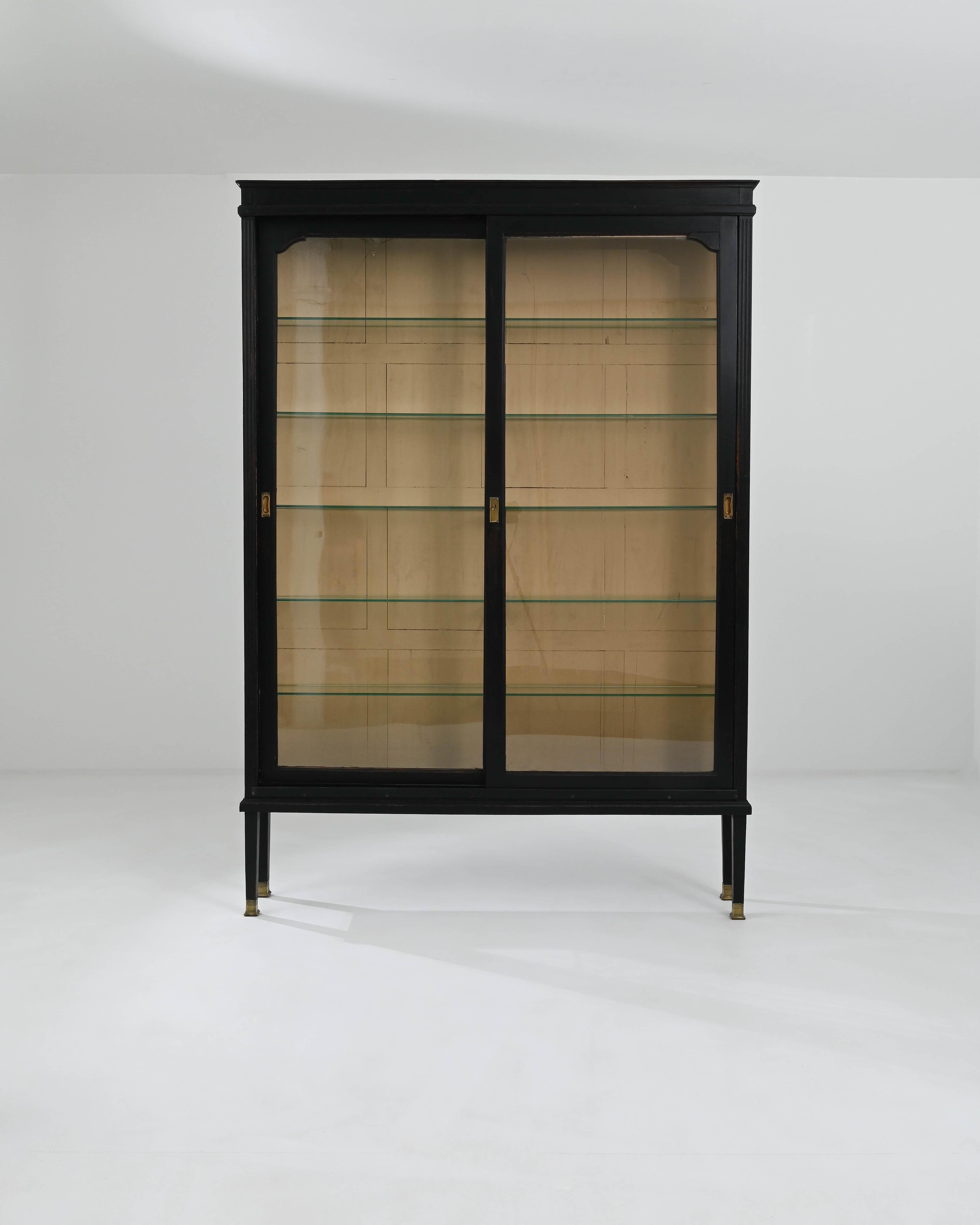 A wooden vitrine created in early 20th century France. This enormous display case proudly displays a bold sense of classic and impressive construction. An elegant glass pane slides away to reveal five spacious shelves, inviting a collection of