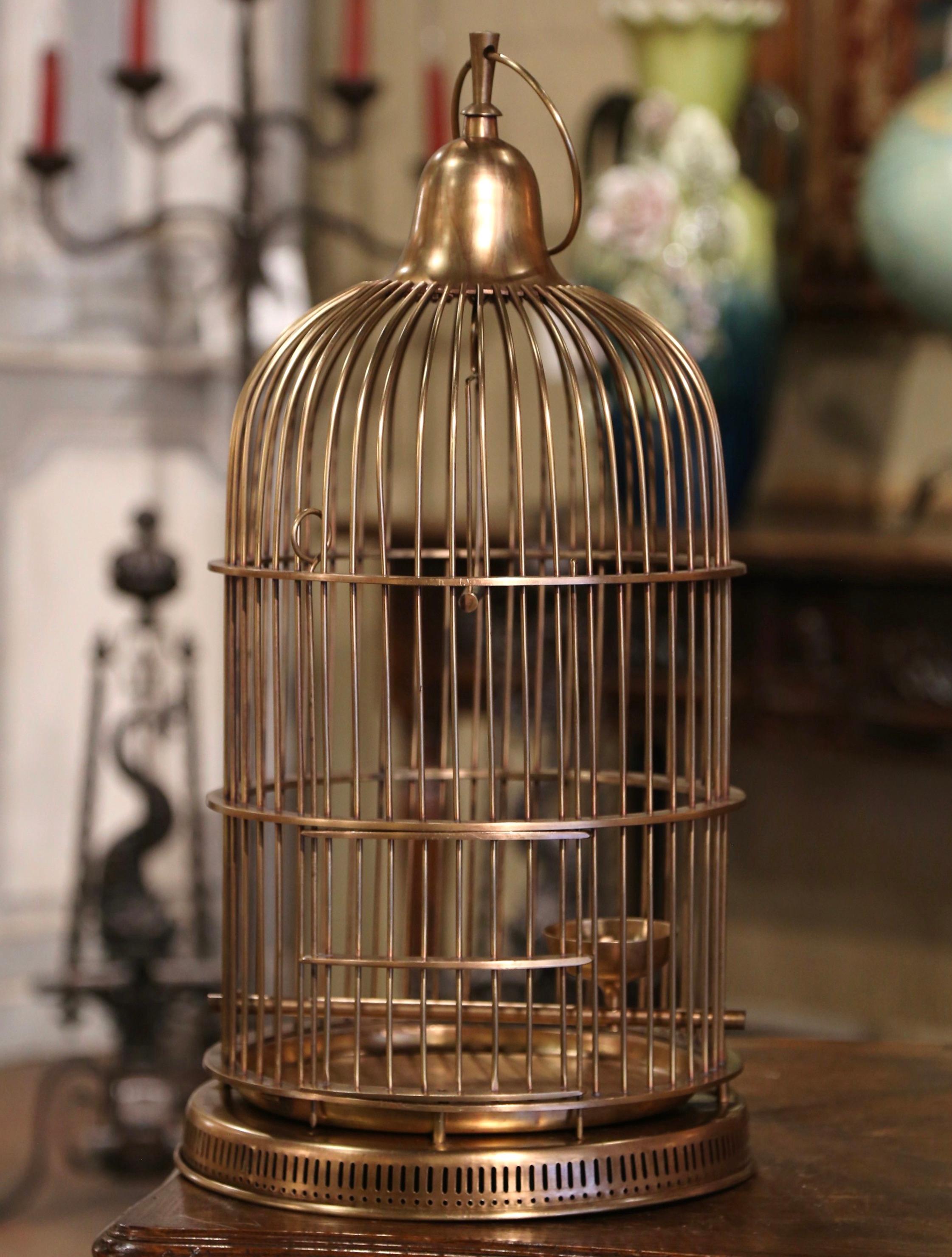 Décorez votre maison avec cette cage à oiseaux antique et fantaisiste. Fabriquée en France, vers 1920, cette cage en laiton, de forme cylindrique, est surmontée d'un dôme arrondi agrémenté d'un crochet de suspension décoratif. La cage dispose d'un