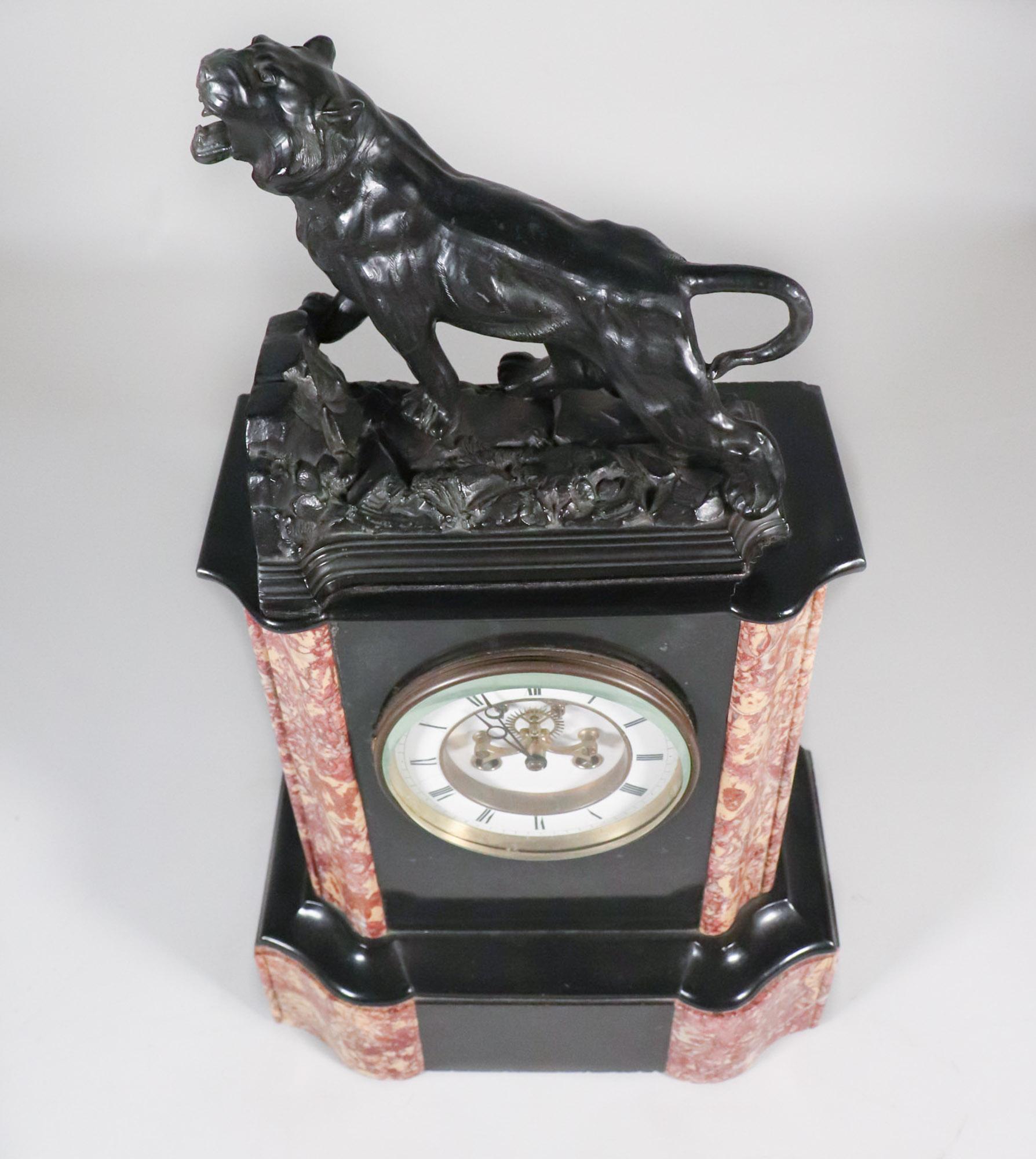 This Circa 1900 French Black Slate and Marble Mantel Clock is a formidable and visually stunning timepiece that commands attention. Atop the clock sits a large, patinated bronze lion, captured in a majestic pose with its mouth open, as if ready to