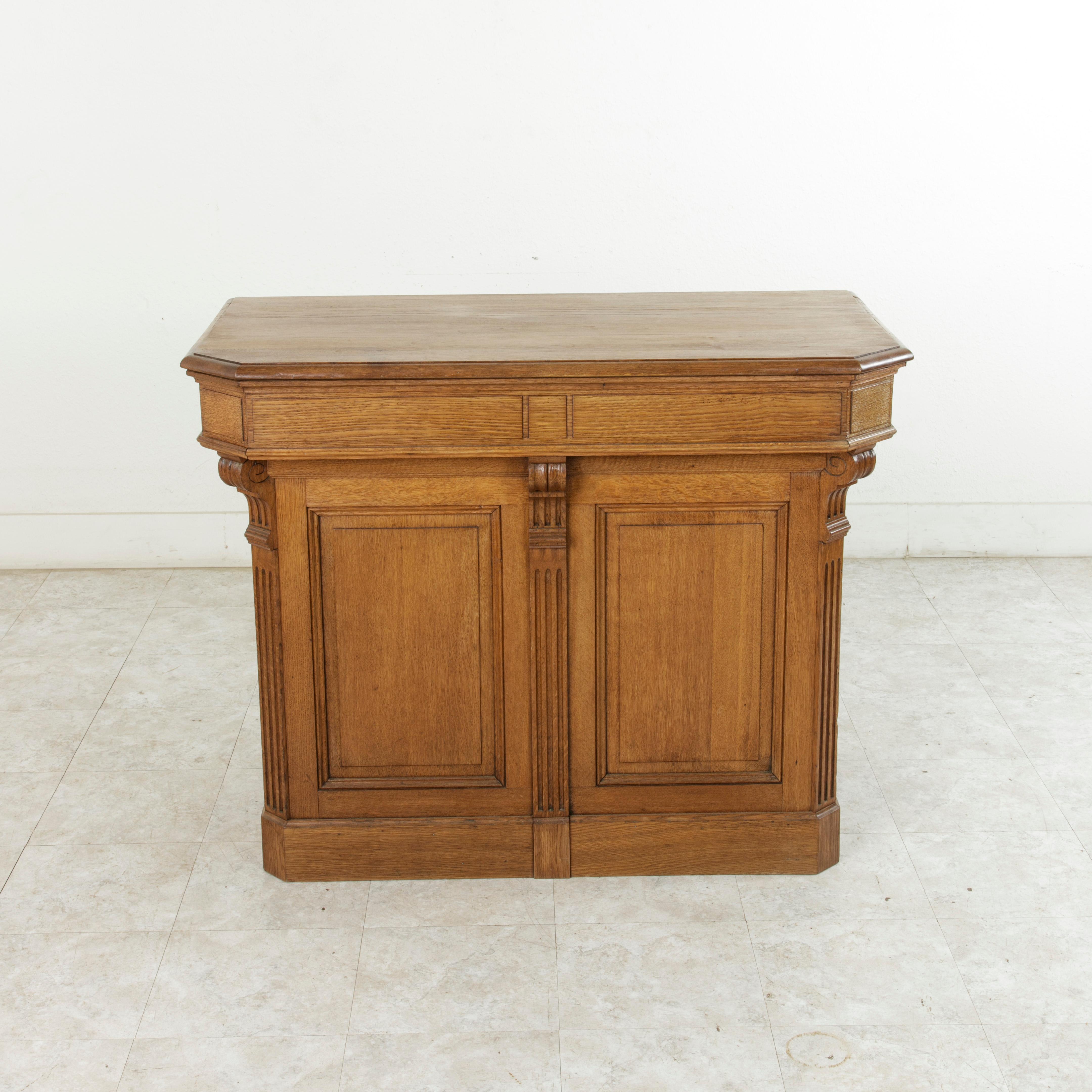 Originally in a French shop, this oak counter or bar features paneled sides and a beveled top. The counter itself stands at 35.5 inches in height from the floor to the top of the work space. Scrolled brackets above the fluted half columns support