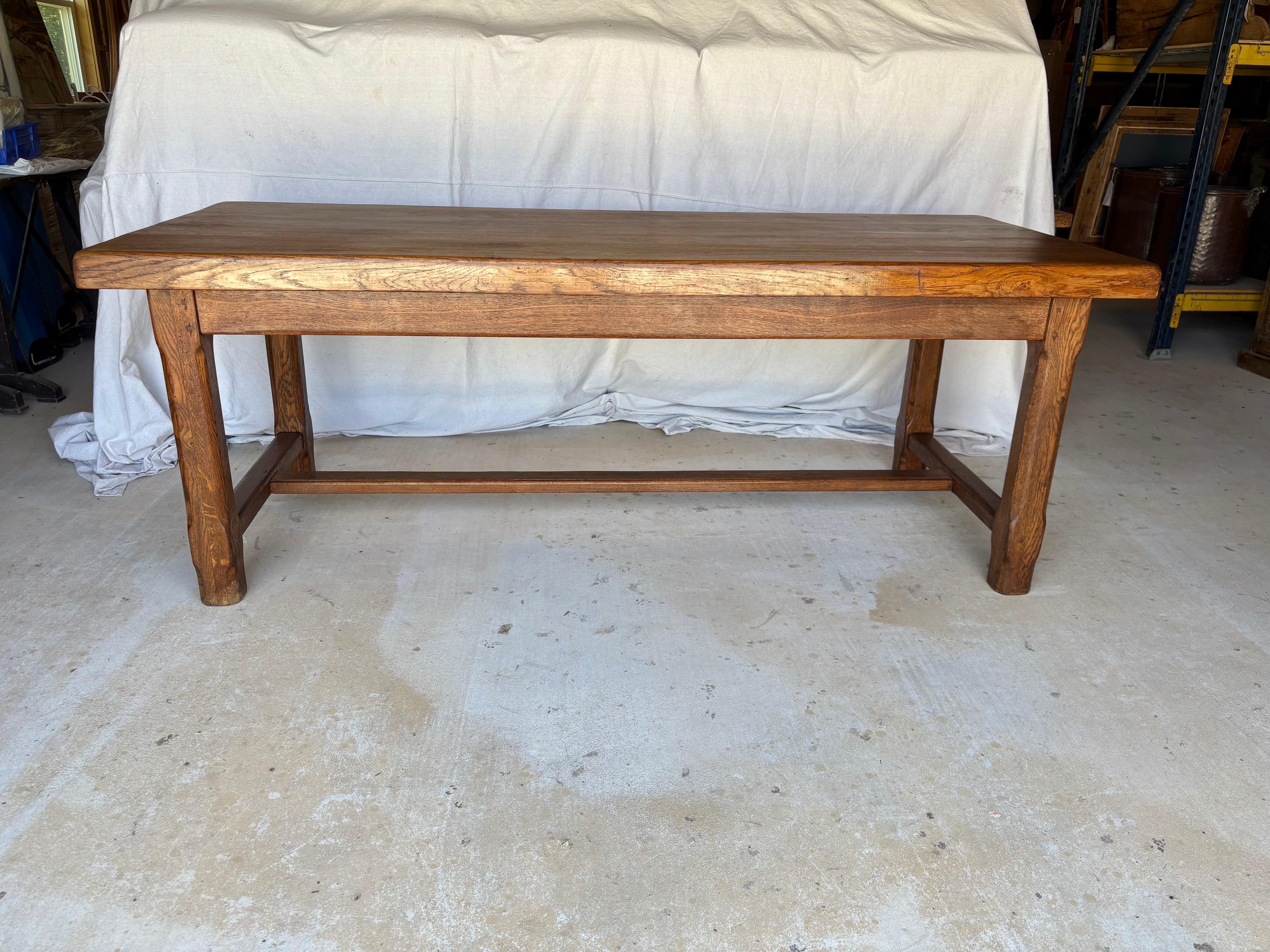 This Early 20th Century Refectory Dining Table was crafted from old growth oak by French artisans in the early 1900's. The piece features wood pegged construction with a dovetailed planked three inch thick top that rest on a sturdy apron leading to