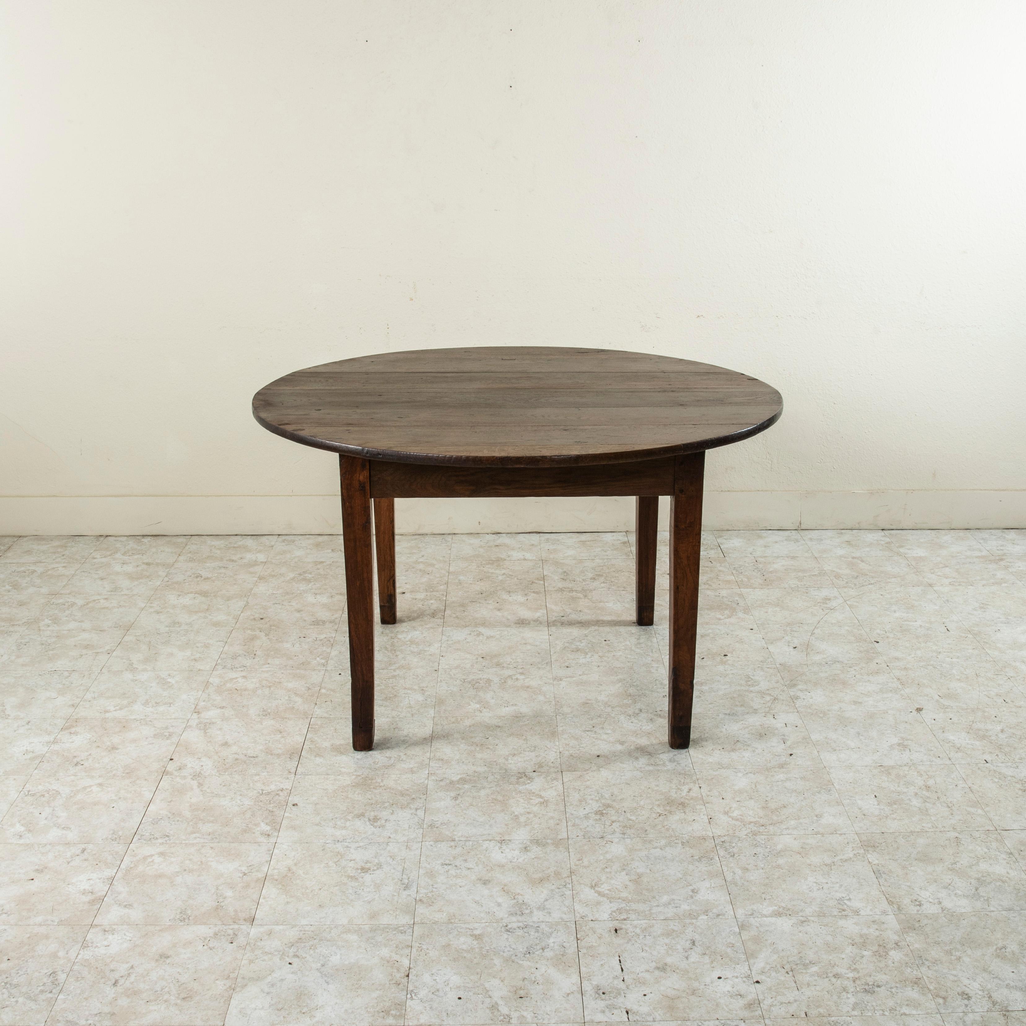 This French artisan made round farm table from the turn of the twentieth century features a solid oak top that measures 51.25 inches in diameter. Resting on a hand pegged oak base of mortise and tenon joinery with four gently tapered square legs,