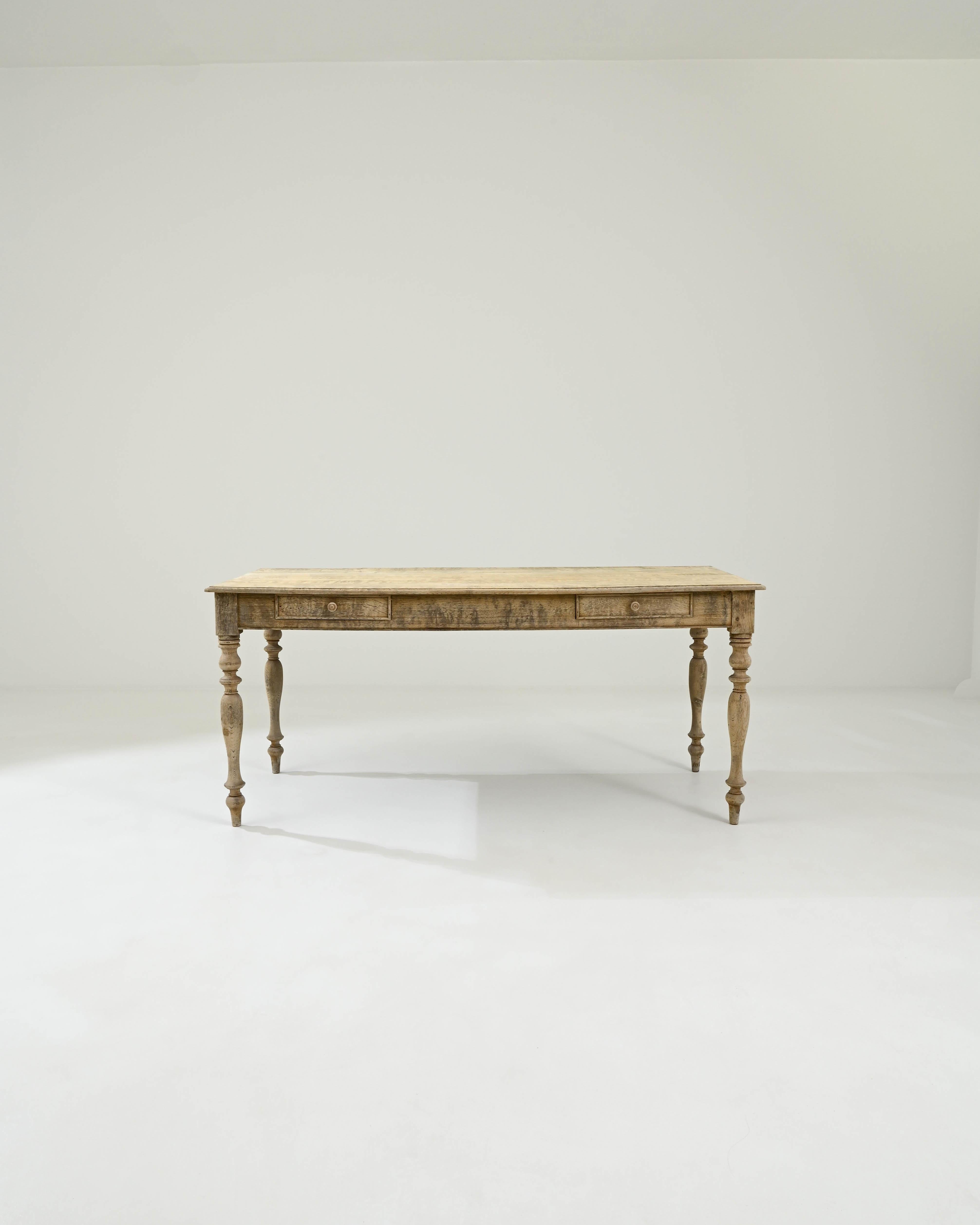 This elegant table was crafted in France, dating back to the 1900s. The simple tabletop rests upon hand-lathed legs, which contribute to a visually pleasing silhouette with their graceful geometric shapes. The large apron features two drawers with
