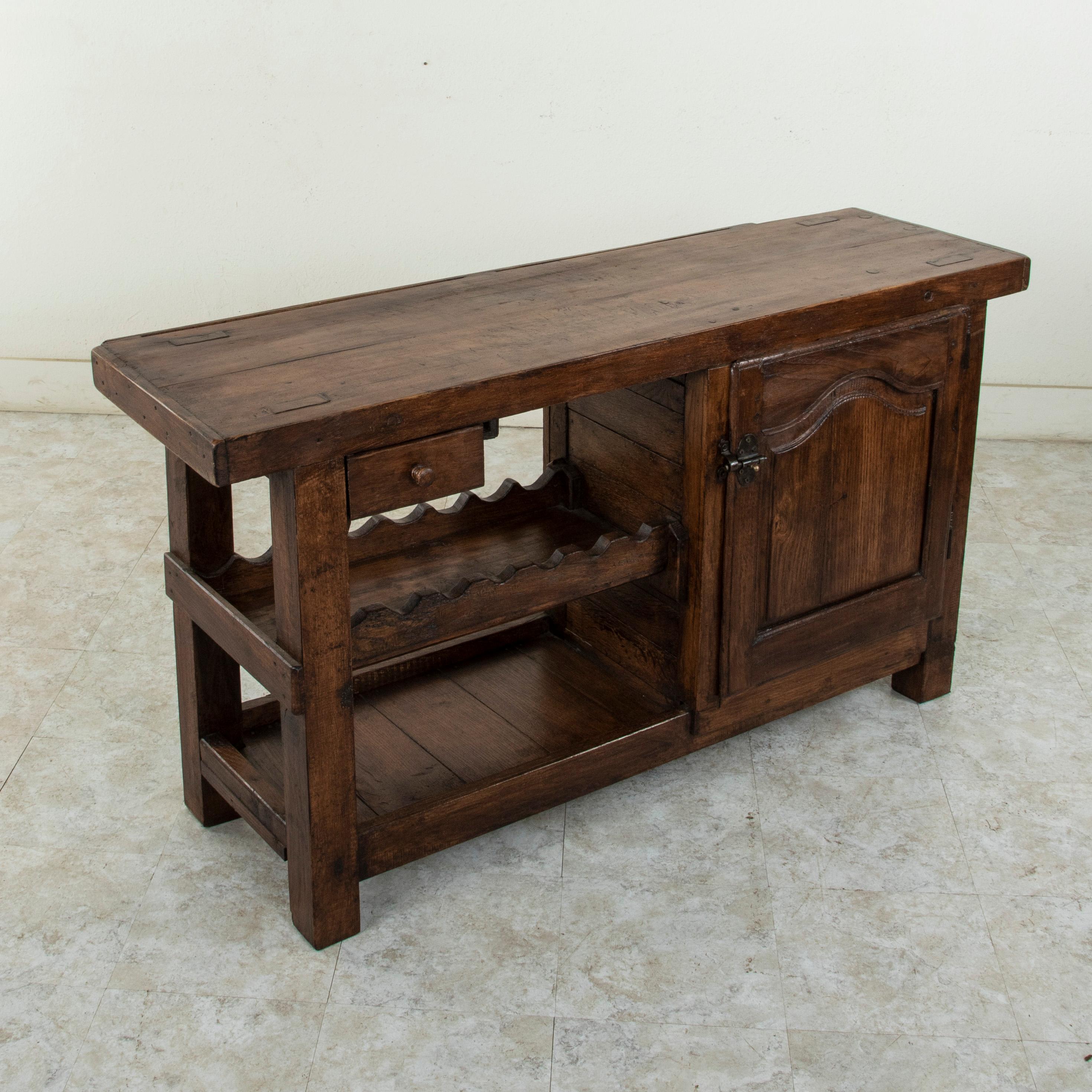 This early twentieth century French oak workbench is from the region of Normandy, France. Two slots at the back of the top once kept the artisan's tools close at hand. Its closed cabinet with single interior shelf, single drawer, and lower shelf