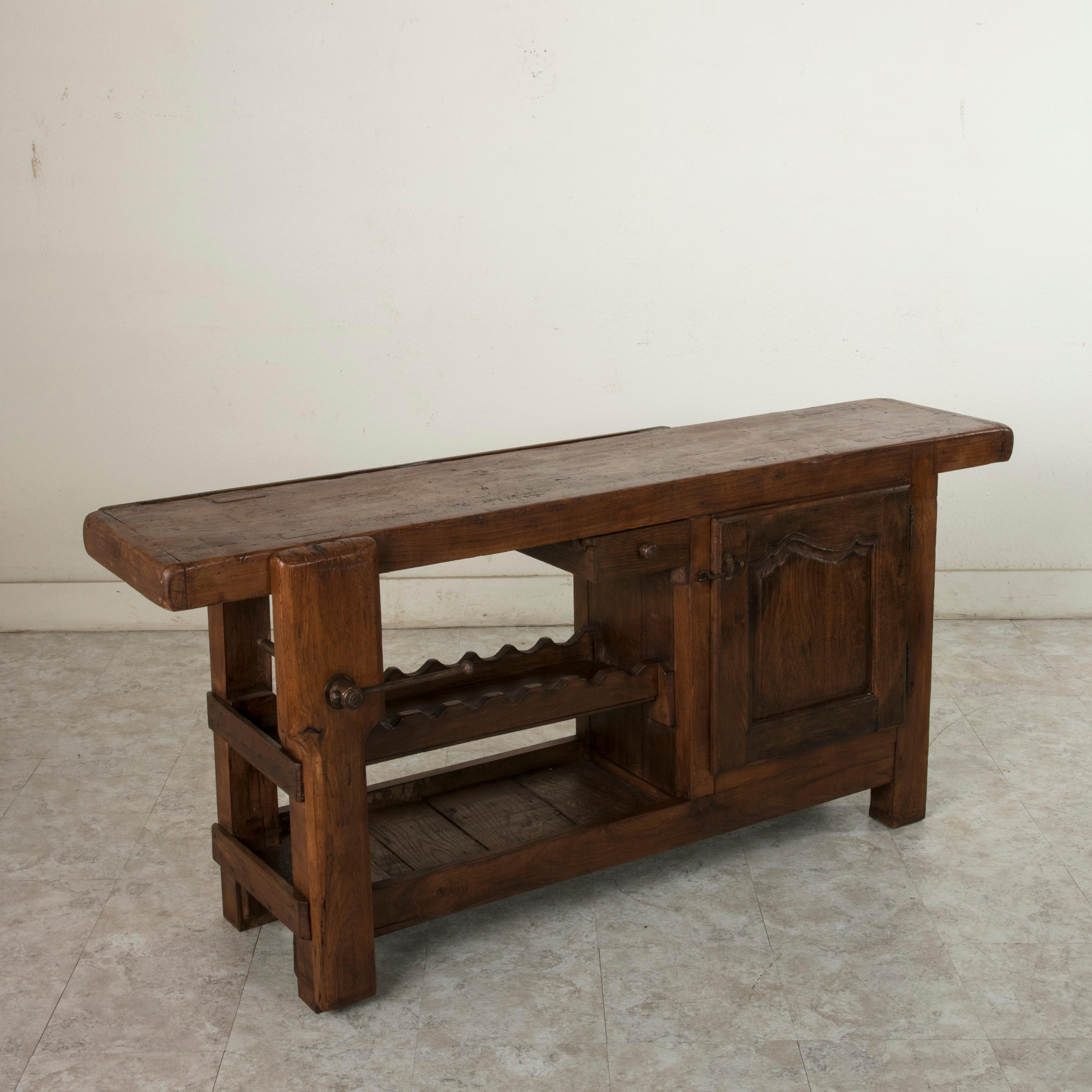 This early 20th century oak workbench is from Normandy, France. Two slots at the back of the top once kept the artisan's tools close at hand. Its closed cabinet with single interior shelf, single drawer, and lower shelf provide ample storage. The