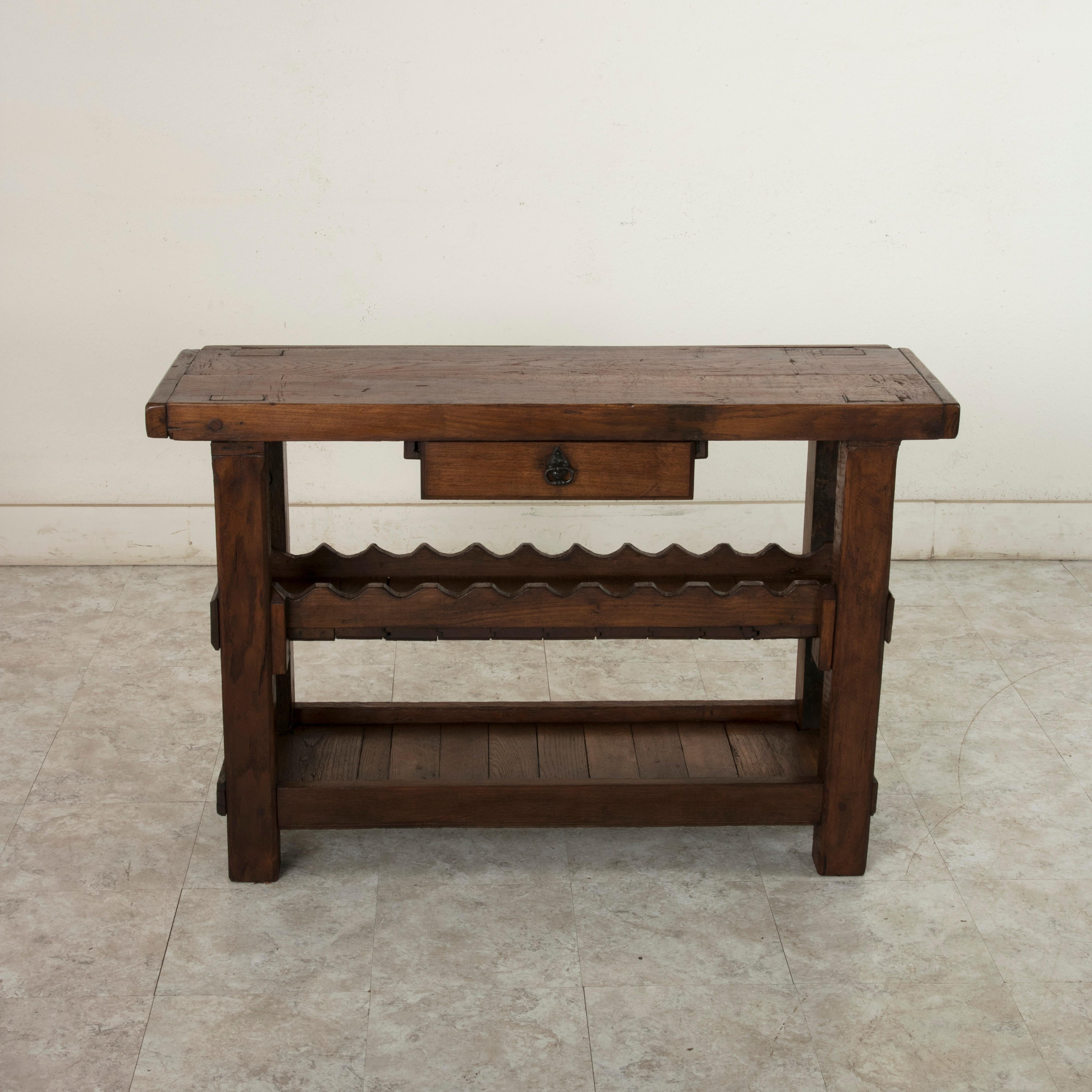 This early 20th century French oak workbench from Normandy, France features a 2.25 inch thick top with a single drawer. Two slots at the back of the top once kept the artisan's tools close at hand. This workbench is constructed using mortise and