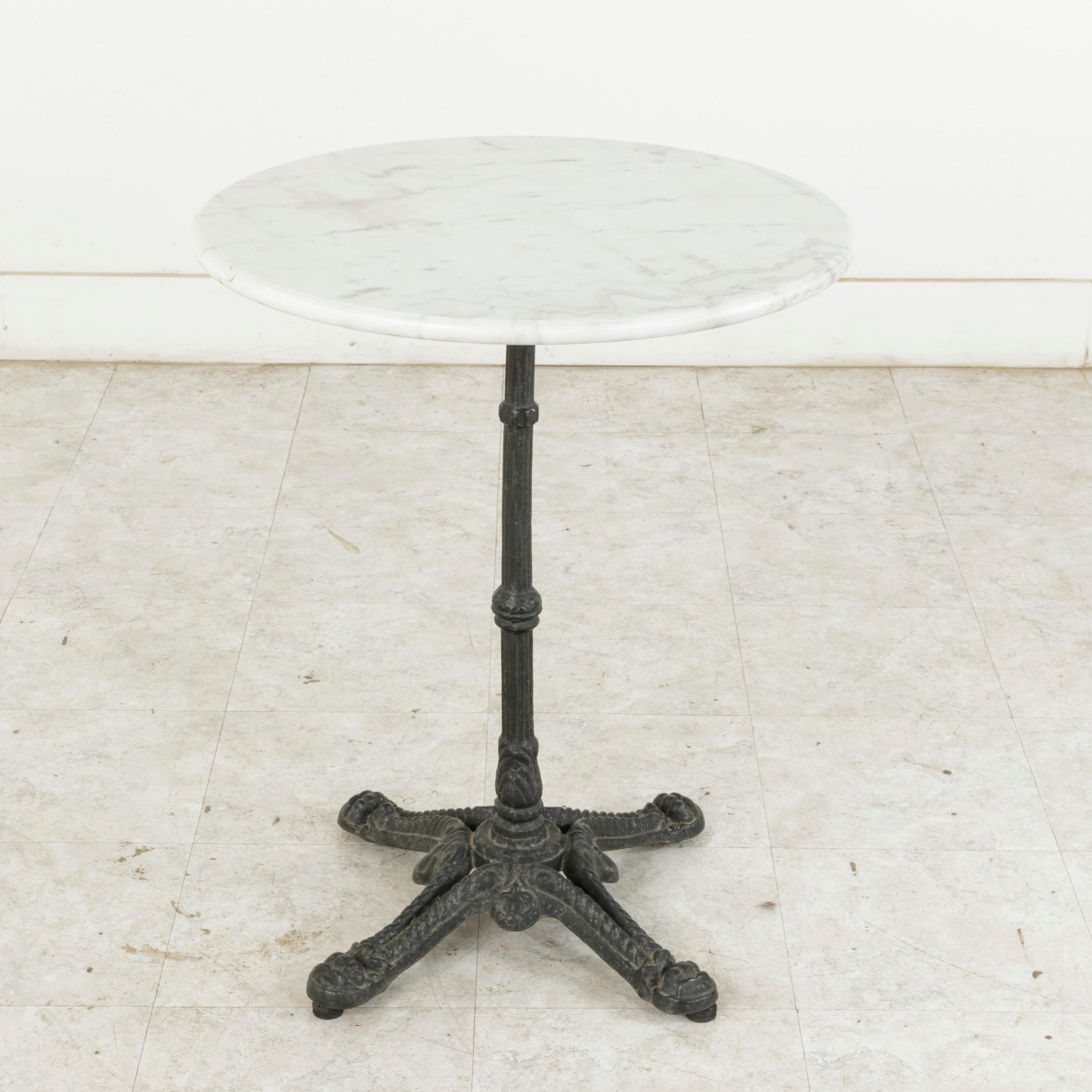 This classic French iron bistro table or cafe table from the early twentieth century features a solid round white marble top with a rounded edge. The top rests on a cast iron base supported by a central fluted pillar. The base is detailed with