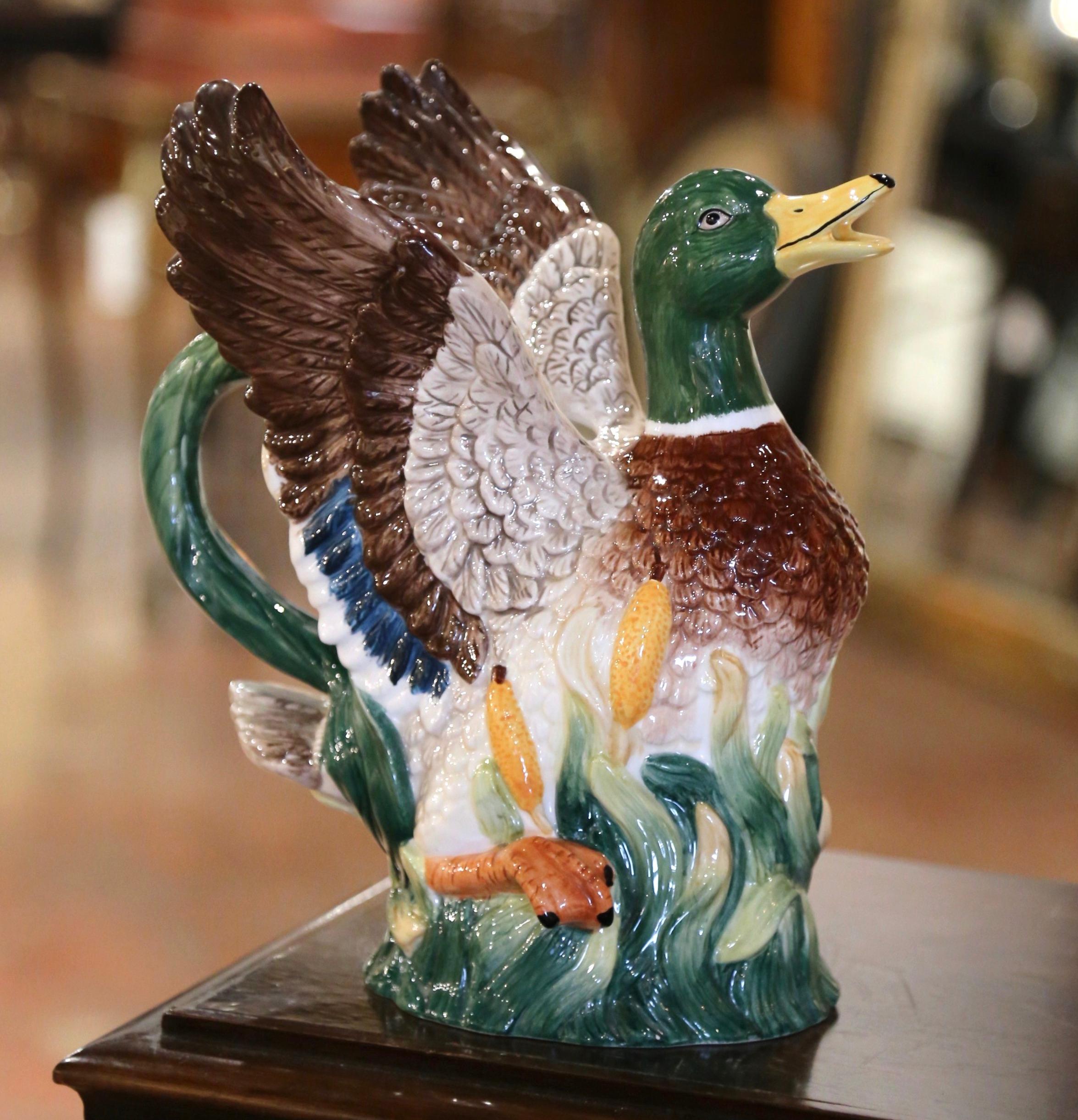 Questa brocca d'acqua in mjolica francese è stata realizzata in Francia intorno al 1920. La brocca raffigura un'anatra domestica in volo, su uno sfondo naturalistico di canne e code di gatto. I colori ricchi e i dettagli intricati fanno di questo
