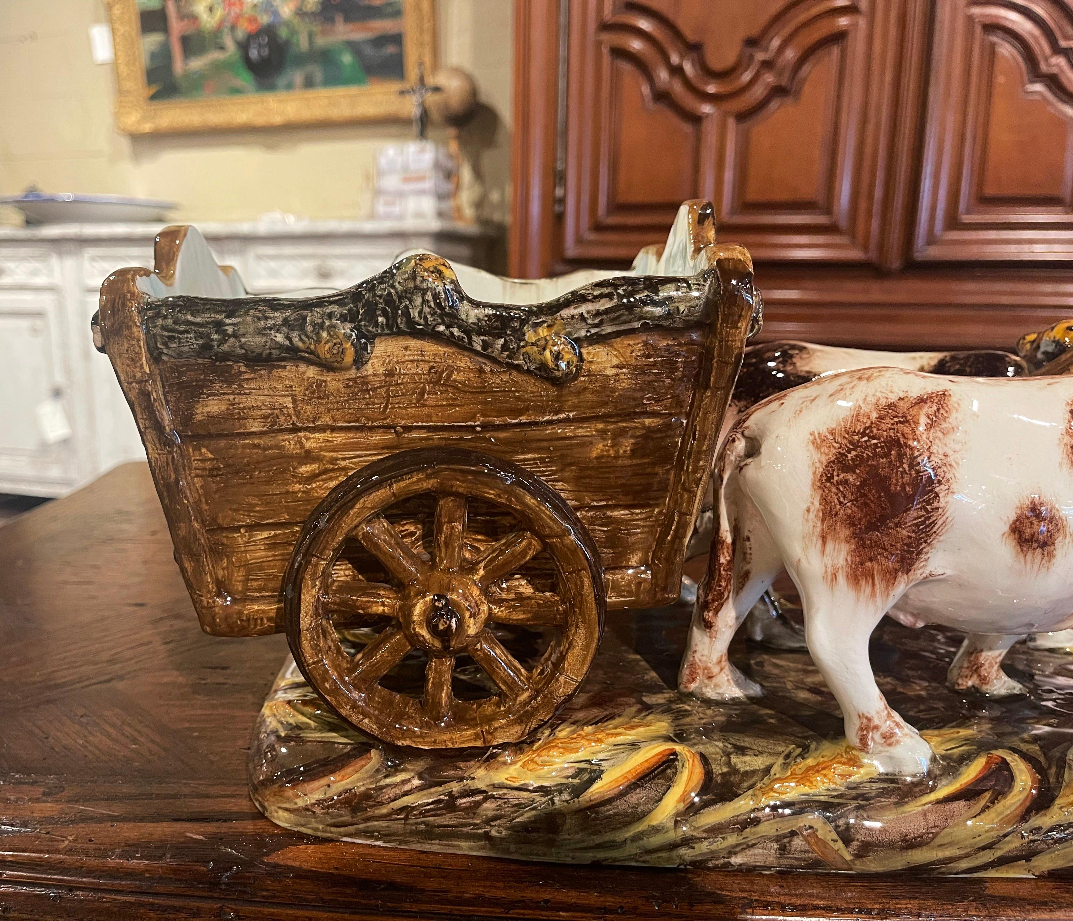 This colorful, antique Majolica sculpture was created on the Riviera of France circa 1920; the composition stands on a green base, and depicts a Classic farm scene with cows pulling a cart. The hand painted ceramic jardinière features a pair of
