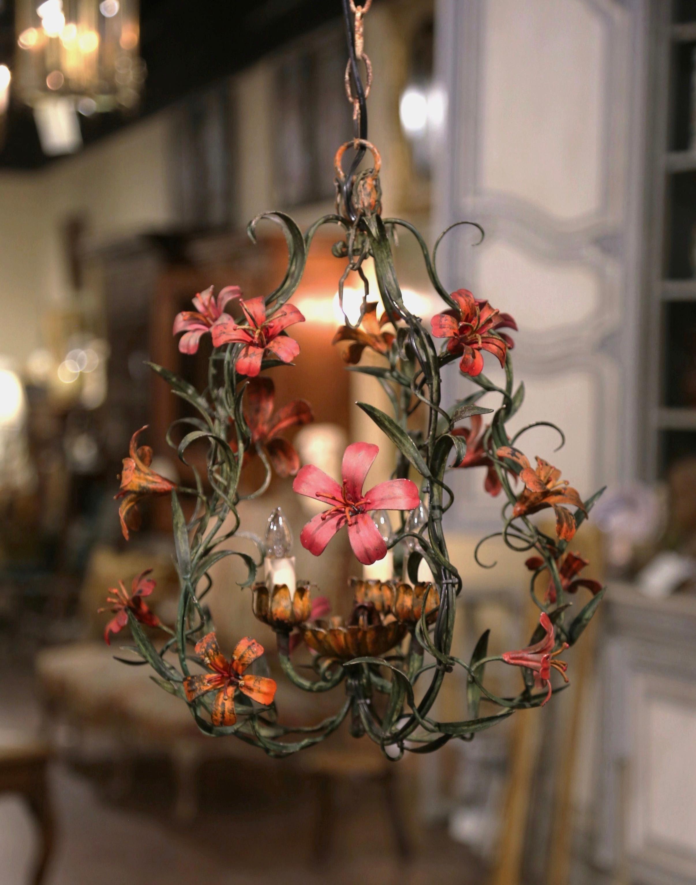 This elegant, antique chandelier was crafted in France, circa 1920. The small, charming hanging light fixture has three lights emerging from blooming tulip-shaped flowers. This antique is further embellished with realistic lily flowers in an orange,