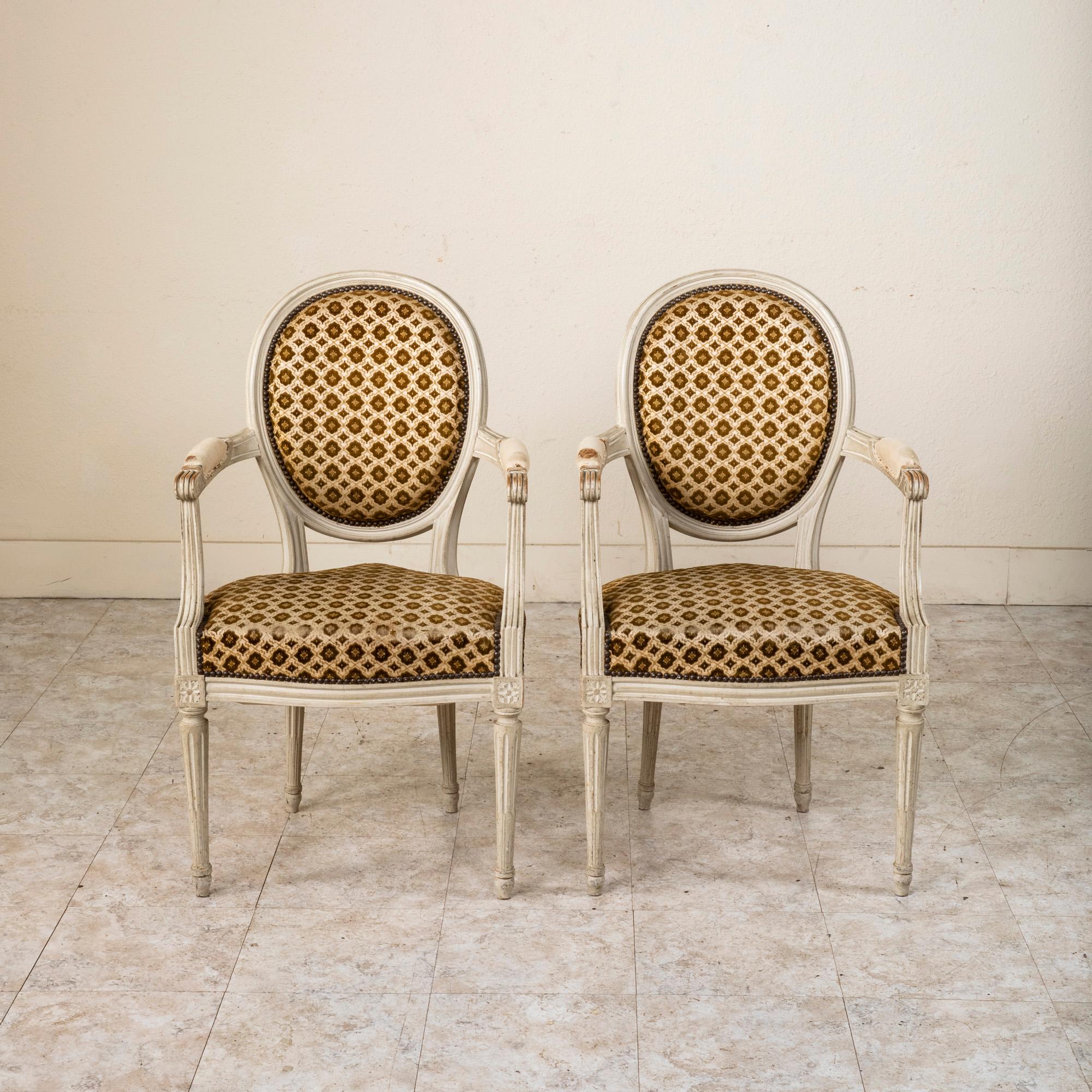 Trouvée en Normandie, France, cette paire de fauteuils cabriolets de style Louis XVI présente une finition patinée d'origine. Cette paire classique présente des dossiers en médaillon, des accoudoirs cannelés avec des accoudoirs à volutes et des