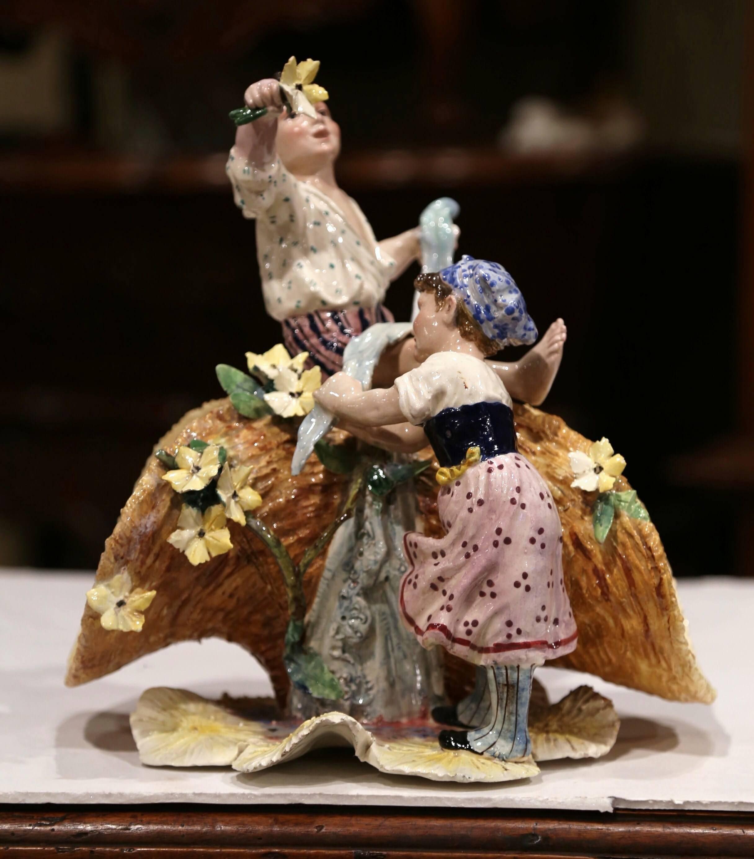 Decorate a shelf with this colorful antique Majolica sculpture composition. Created in France, circa 1920, the porcelain vase features two young children, a boy siting on the basket and a girl standing by. The composition is further decorated with