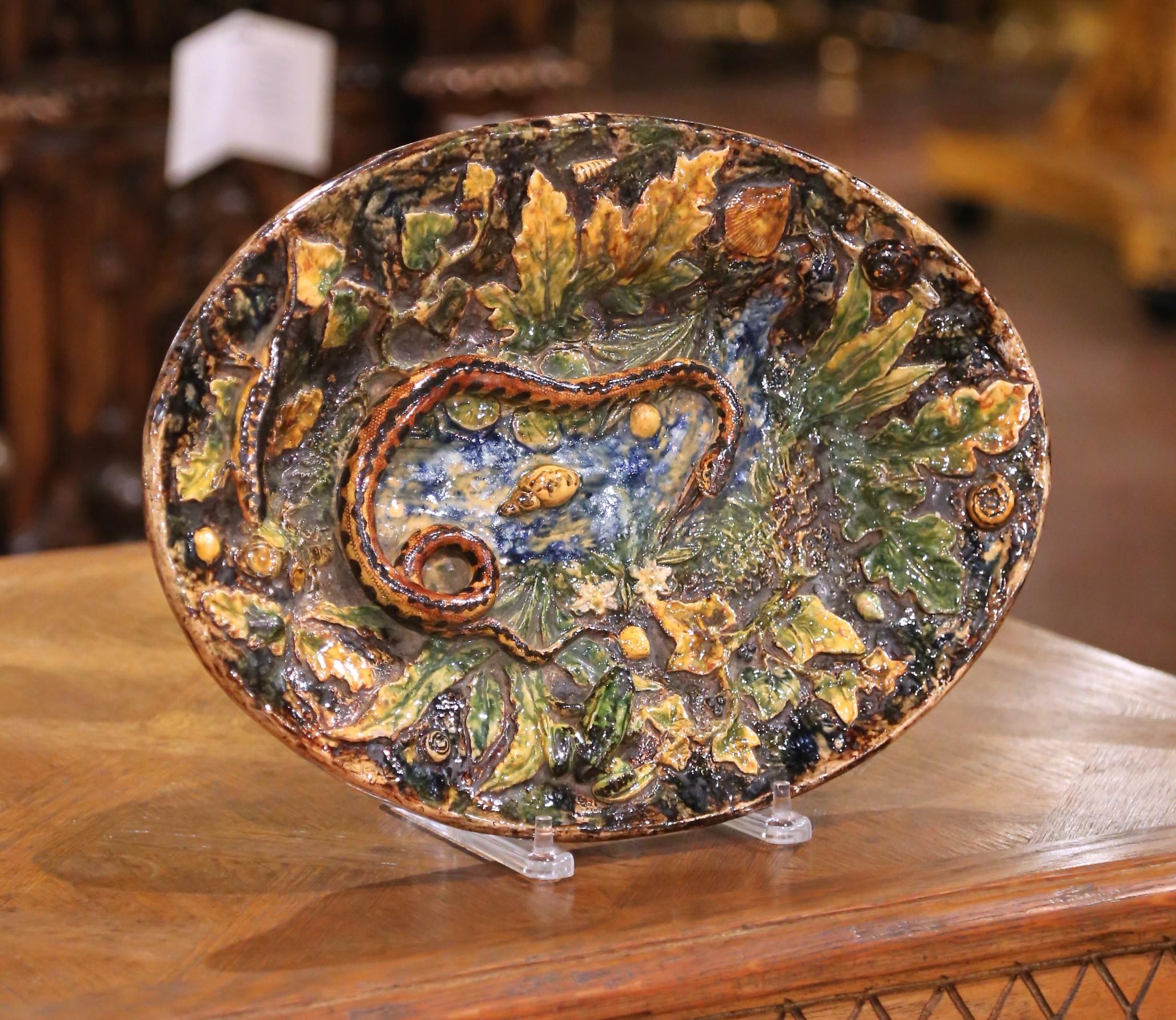 Questo piatto in maiolica in stile Palissy francese dei primi del Novecento, ricco di texture, colori e movimento, dà vita al mondo naturale in un vivido rilievo. Al centro, un serpente arrotolato si snoda in una palude vivace, circondato da rane,