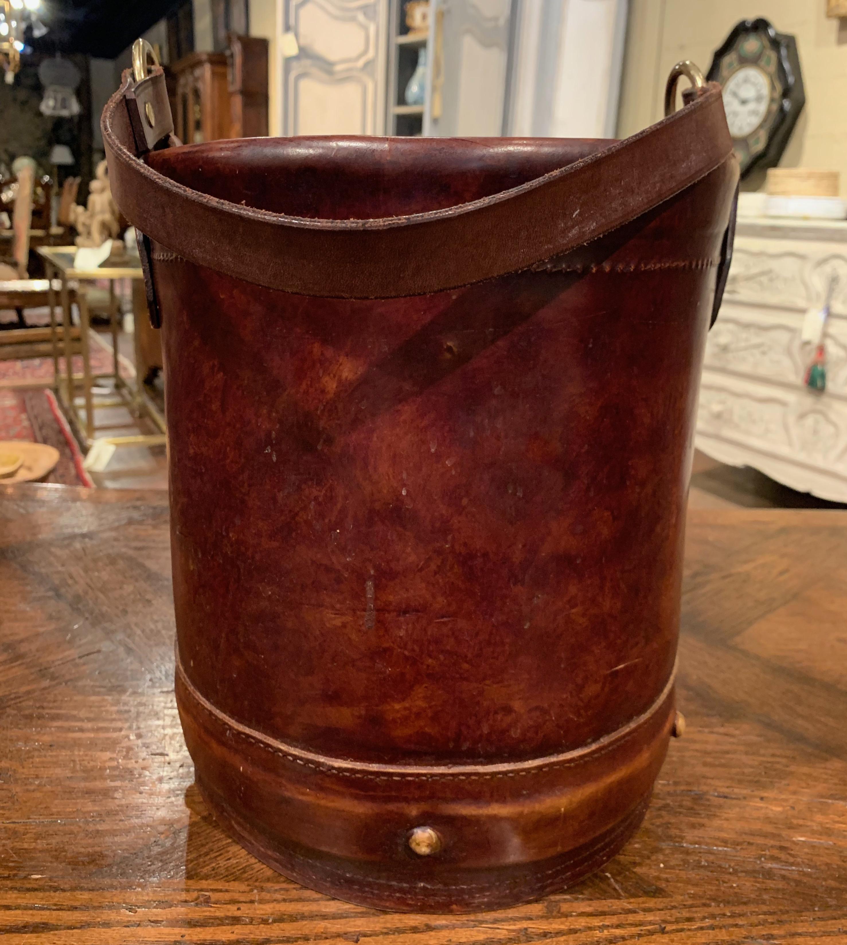 Crafted in France circa 1920, the antique decorative basket is round in shape and is embellished with a strap decorated with brass rings and brass nail heads around the base. The waste basket is in excellent condition with a rich patinated