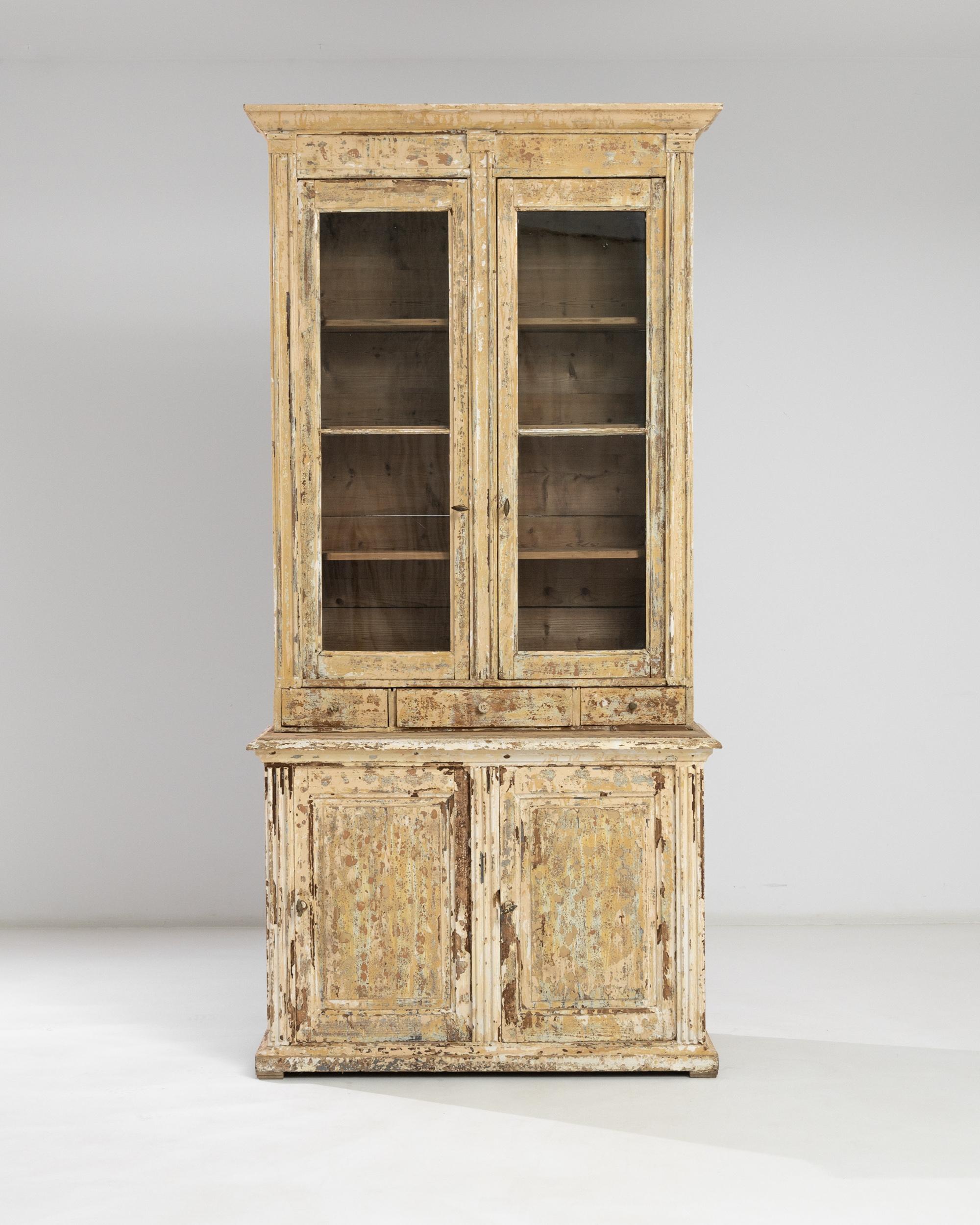 This statuesque vitrine crafted in France in the early 20th century impresses with the unique patchy texture of the original patina that accentuates bold outlines of the chest: the raised doors of the lower compartment adorned by flute side
