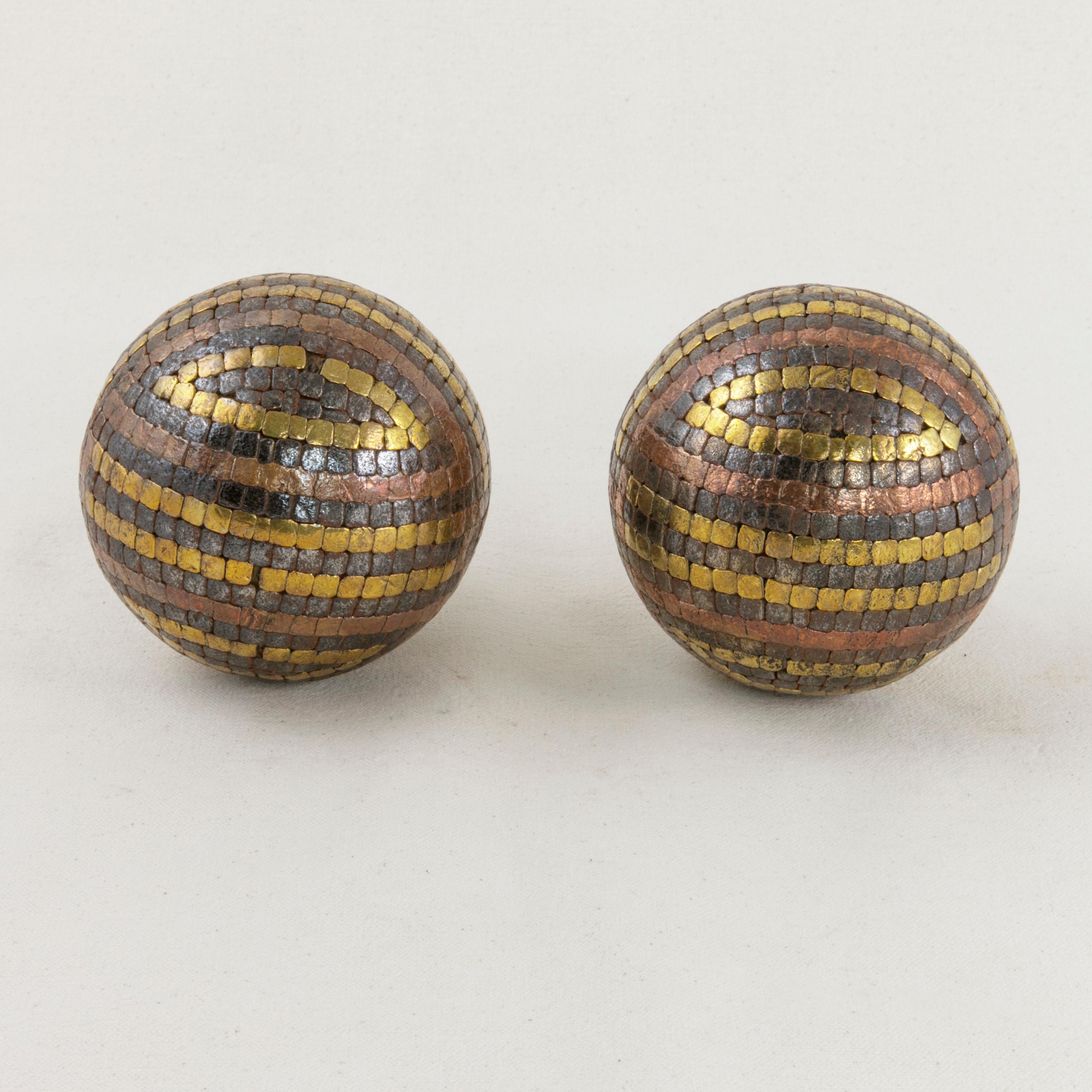 This pair of French artisan-made petanque balls from the early 20th century features copper, brass, and iron stud nails that form a cross pattern around its wooden core. Petanque is a lawn ball game played in the south of France much like bocce ball