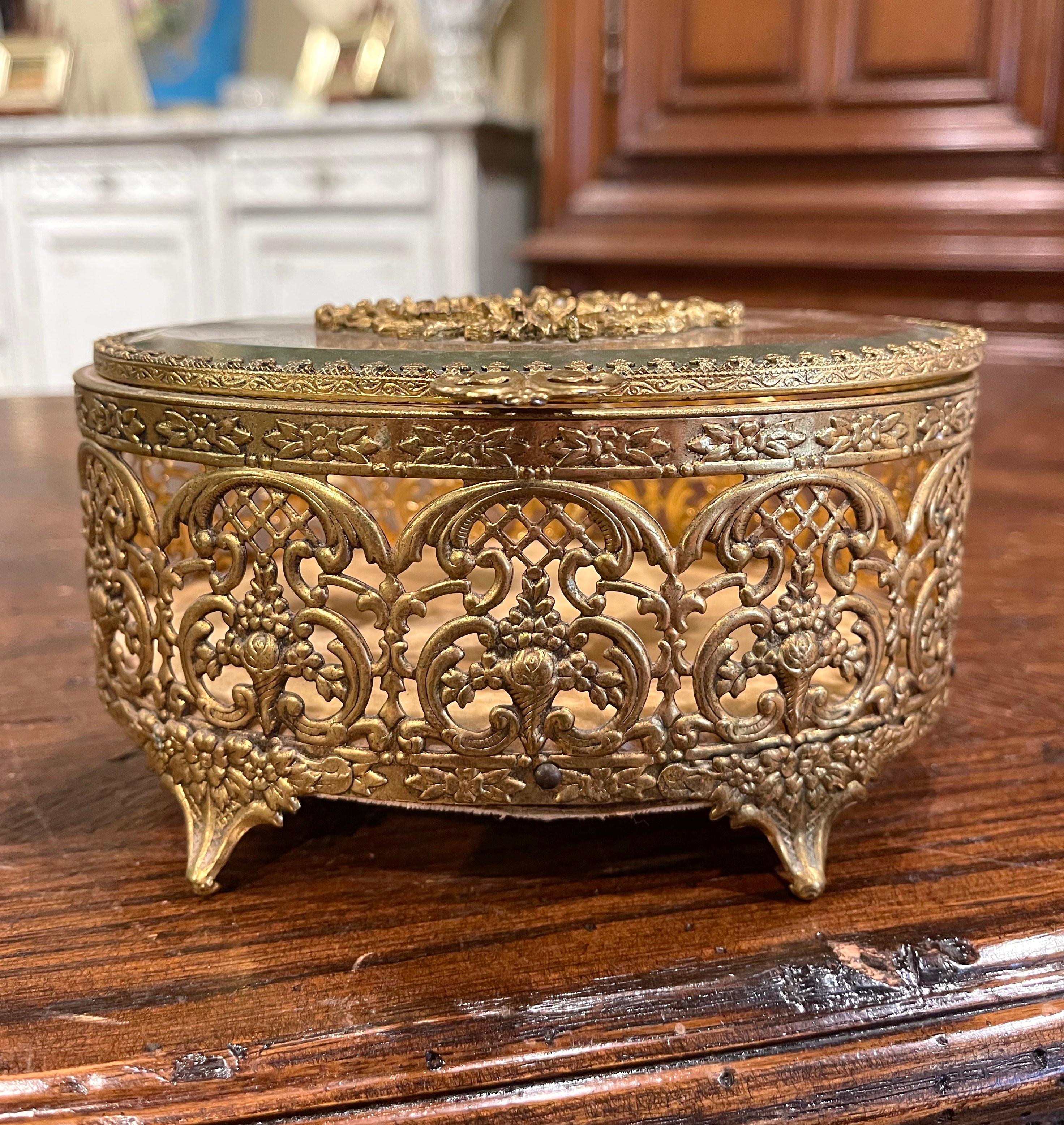 Keep your jewelry or other valuables in this delicate antique box. Crafted in France circa 1920, the box is oval in shape and stands on small curved feet; the pierced brass casket is decorated with floral motifs over a beveled glass top embellished