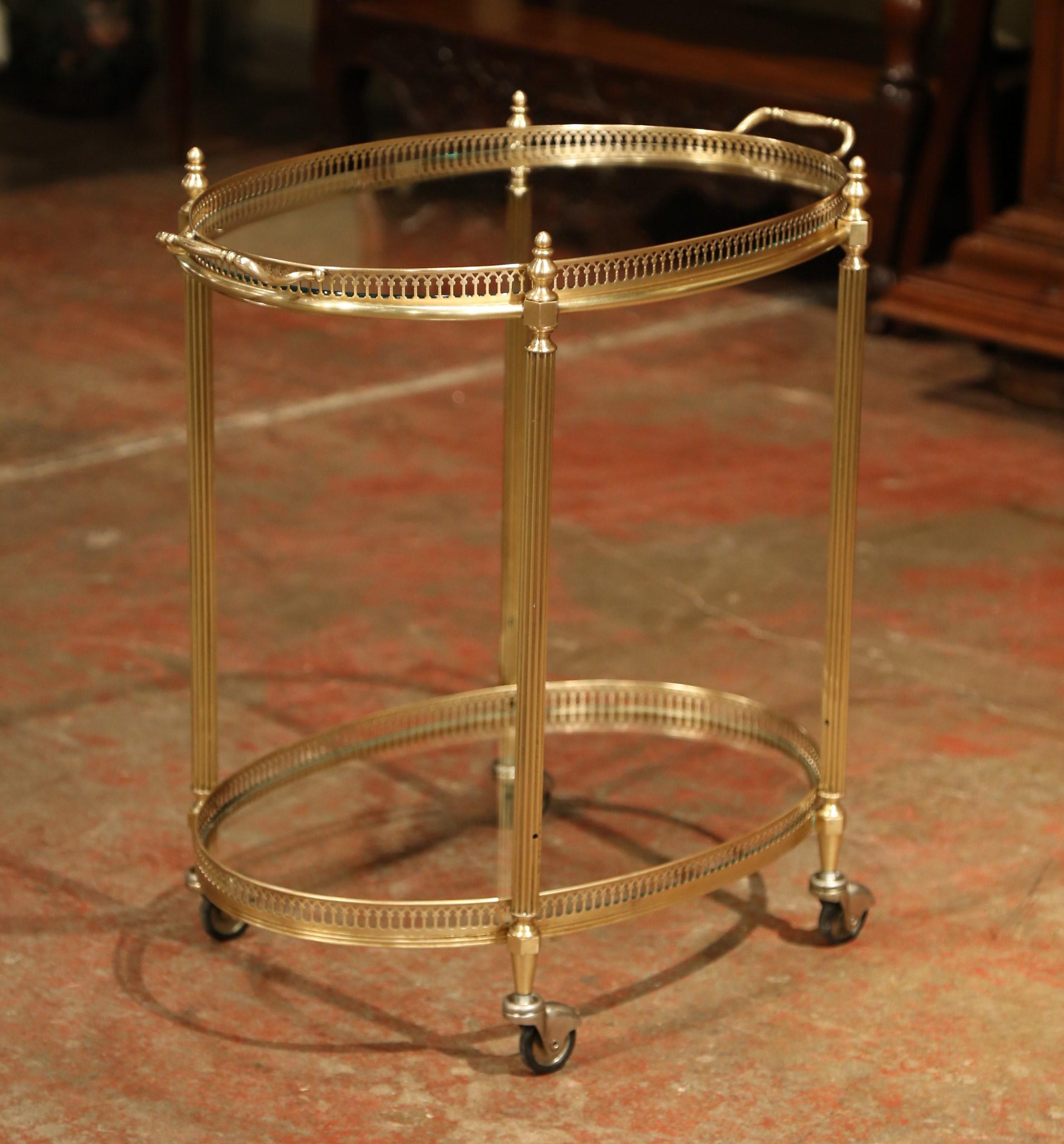 This beautiful, vintage two-tier rolling bar cart was created in France, circa 1930. The dessert table has a brass frame, small round wheels with rubber tires, and two plateaus topped with glass surfaces. The top deck features a removable tray with