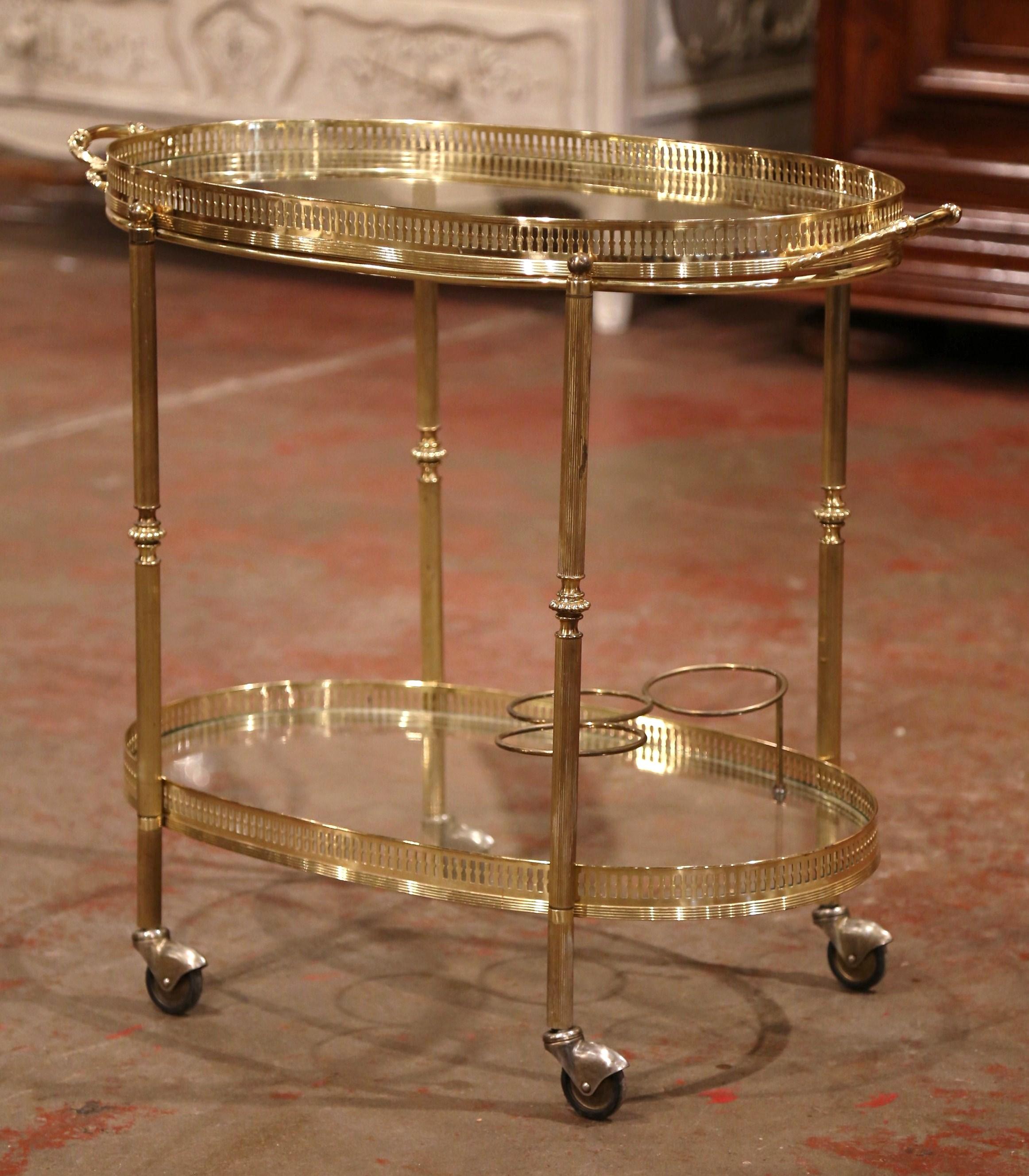 This beautiful, vintage rolling bar cart was created in France, circa 1930. Oval in shape, the brass dessert table stands on four legs finished with small round wheels with rubber tires, the table features two plateaus topped with glass surfaces and