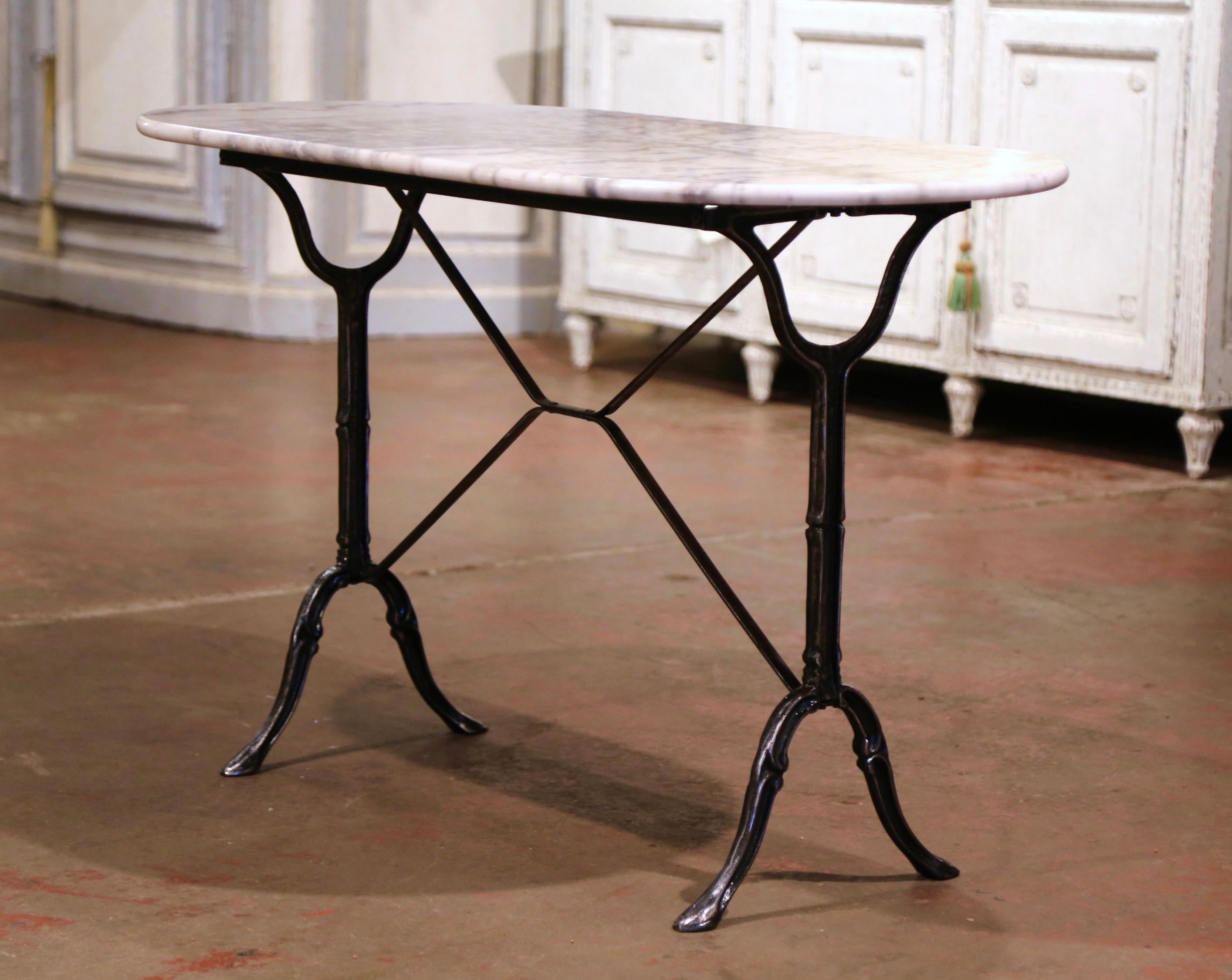 Crafted in France circa 1920, the antique cast iron table sits on a trestle base with elegant scroll legs, joined with a double decorative stretcher. The piece is dressed with the original oval white and grey veins marble top. The classic French