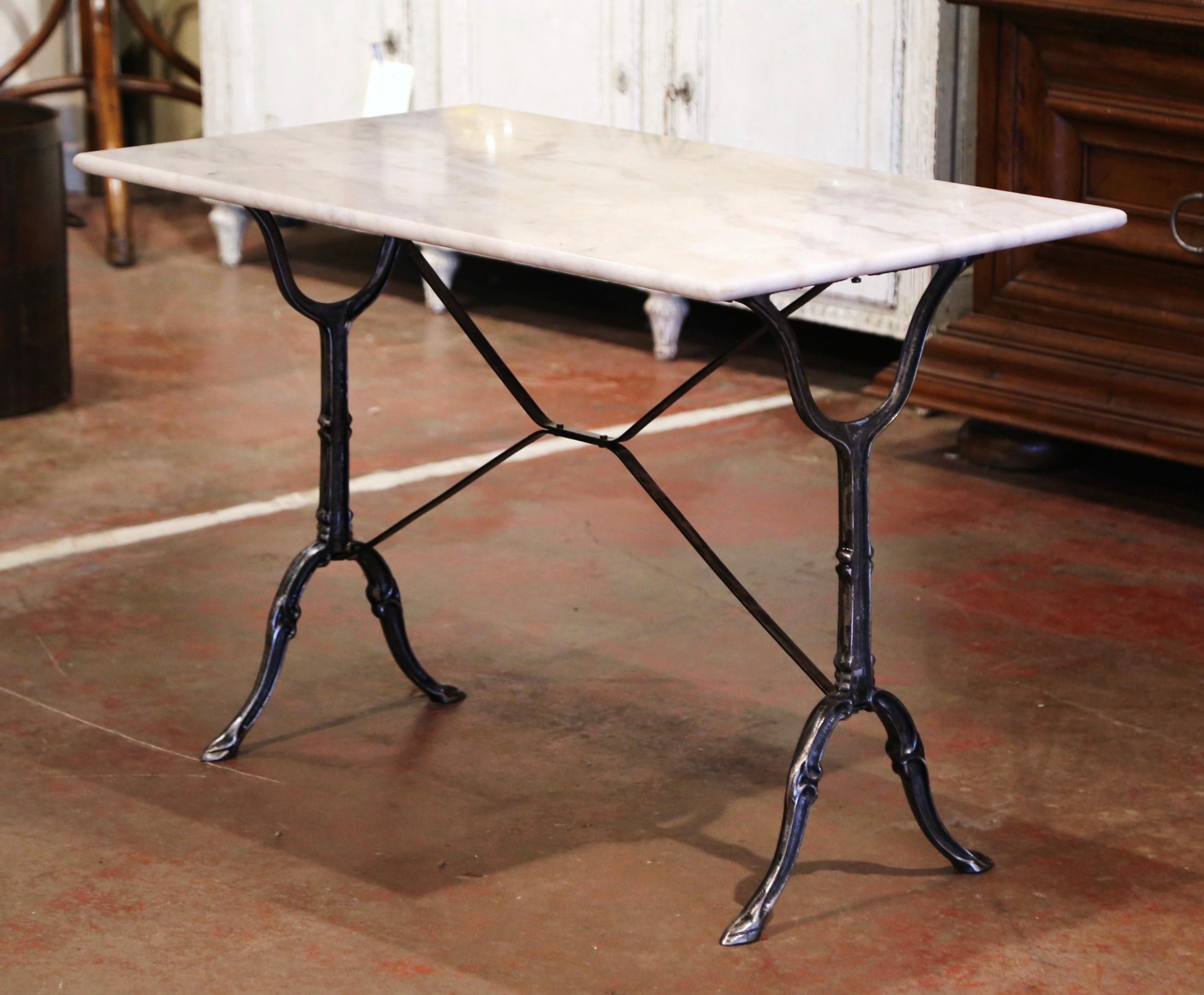 Crafted in France circa 1920, the antique cast iron table sits on a trestle base with elegant scroll legs, joined with a double decorative stretcher. The piece is dressed with the original rectangular white and grey marble top. The classic French