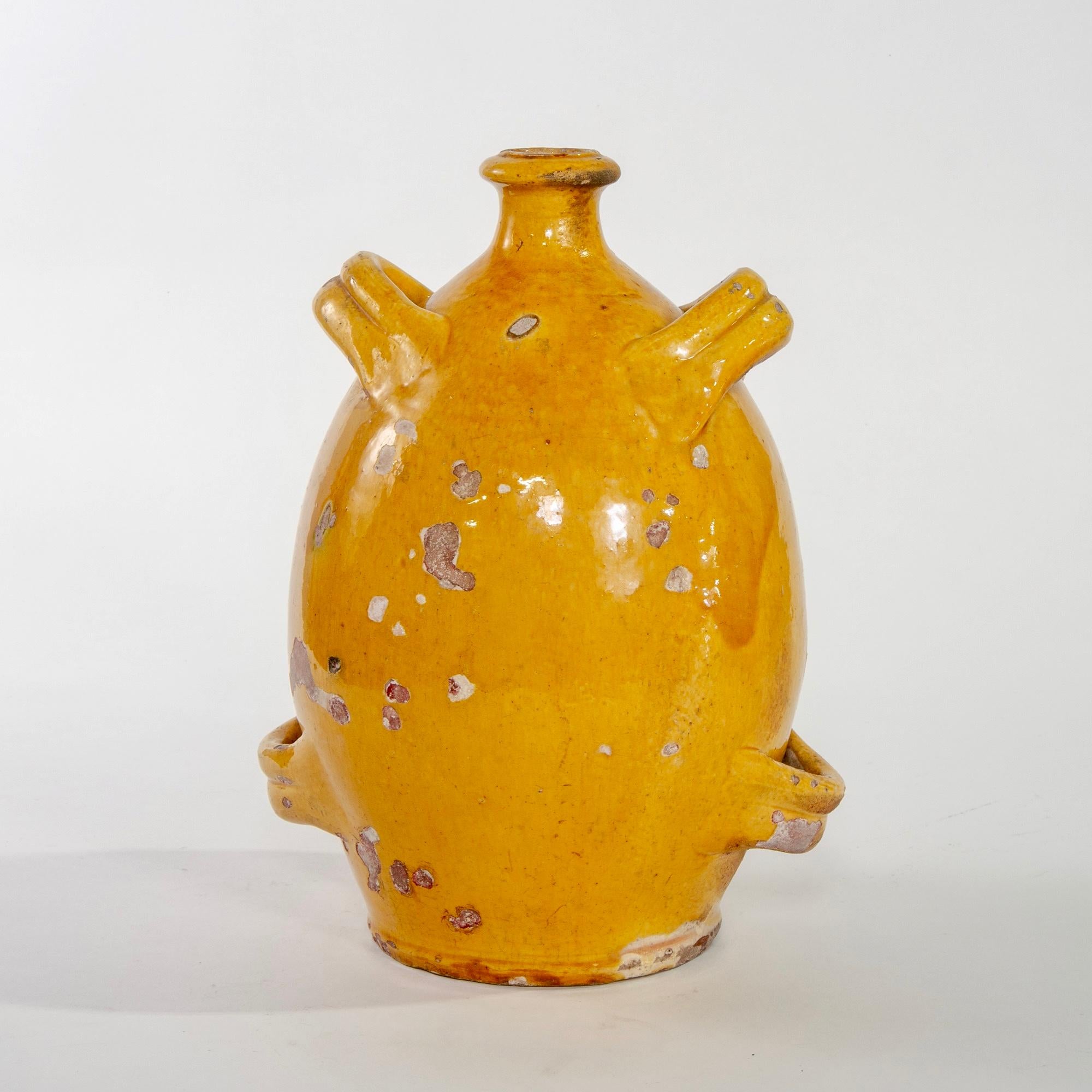 Tall French ceramic jug has four handles, narrow neck and a mustard-gold color glaze, circa 1920s. Vessel stands just under 12” high and body has scattered flakes and chips to glaze.