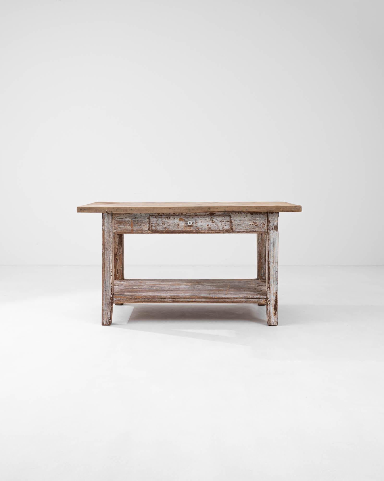 The simple, hard-wearing form of this vintage provincial side table has a timeless appeal. Hand-built in France in the early 20th century, a tabletop of thick wooden boards sits atop a sturdy frame. A lower storage platform and a small drawer set