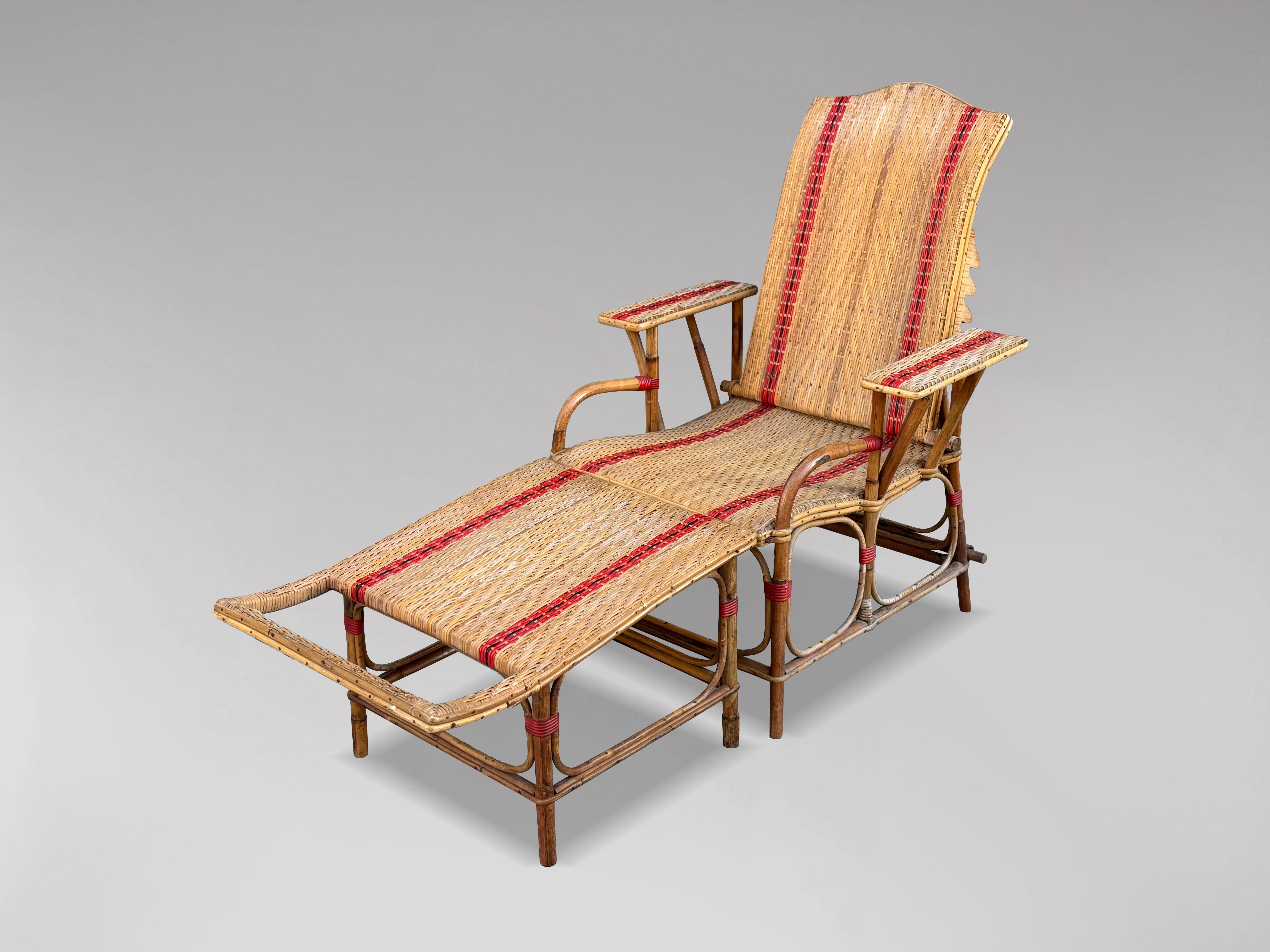 This early 20th-century French Riviera bamboo and rattan reclining chaise longue sun lounger is a stunning example of French design. The piece features a bamboo structure with a braided wicker back and seat, accented by a striking red outline, along